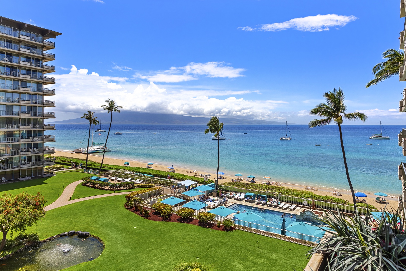 Beachfront resort with pristine pool overlooking turquoise waters and sandy shore under brilliant blue skies.