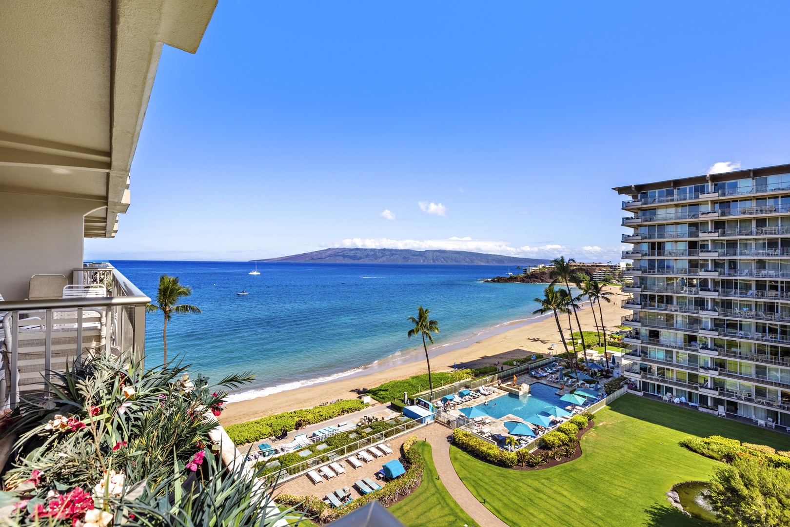 Elevated panorama of Kā‘anapali Beach with lush resort grounds, a sparkling pool, and turquoise ocean stretching to the horizon.
