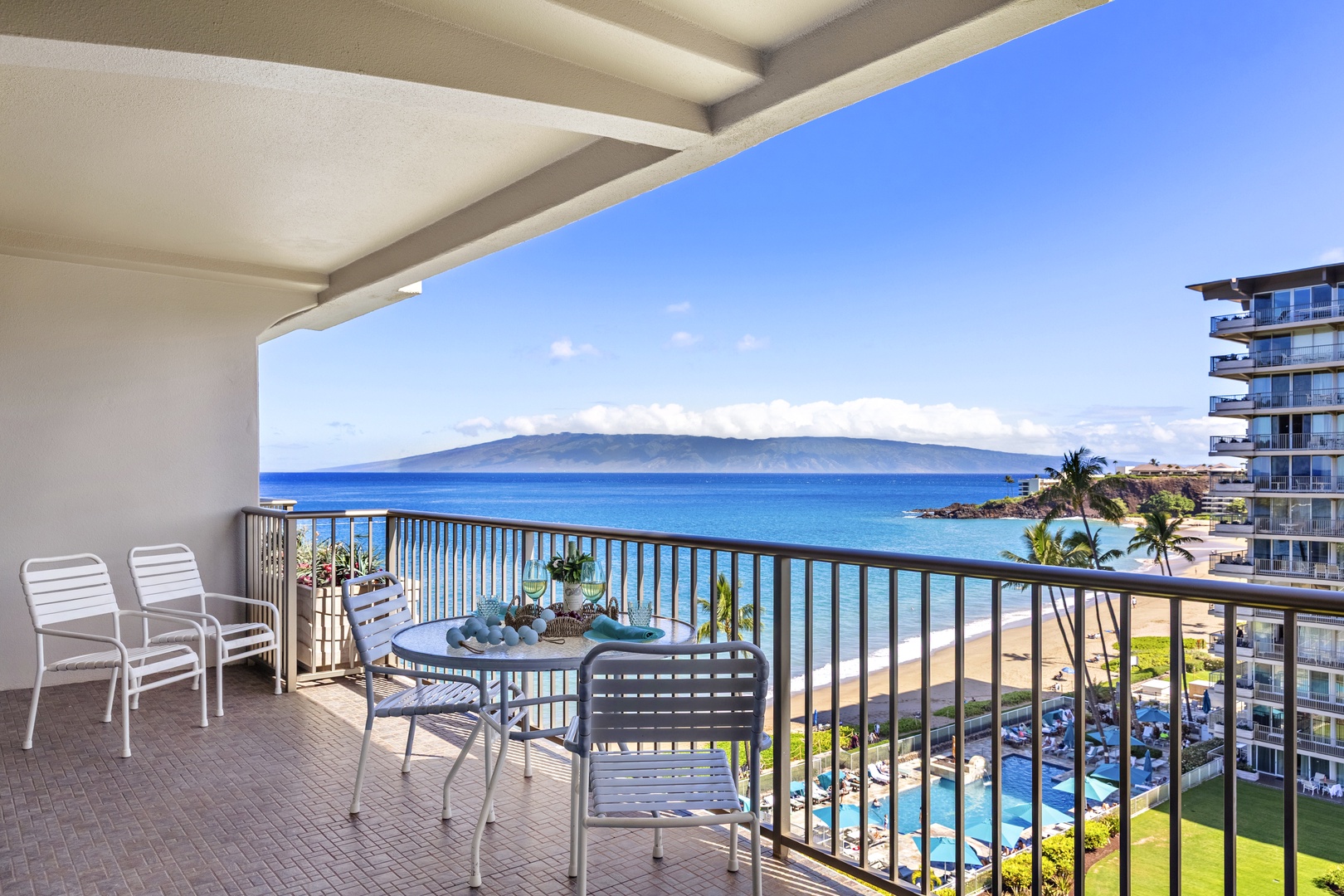 Breezy private lanai with seating for two, overlooking vivid blue waters and a sweeping coastline view.