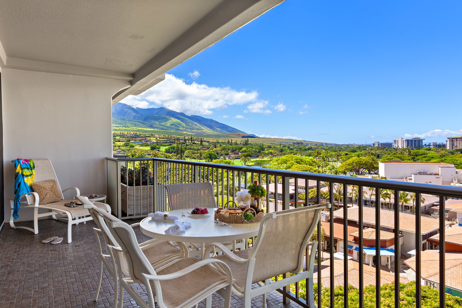 Expansive balcony with mountain and valley views features outdoor dining for four and lounge seating under covered shade, perfectly positioned for sunrise coffee or evening relaxation.