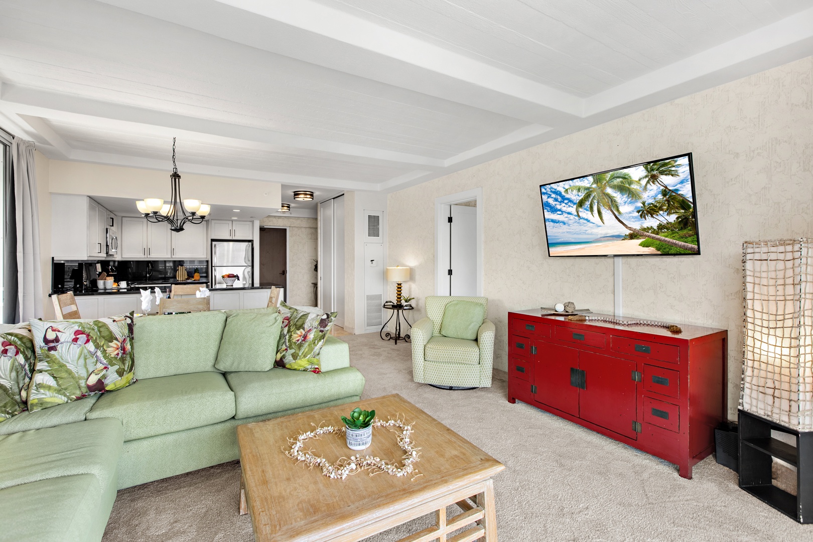 Relax in your spacious, light-filled living area where soft green sofas and tropical accents create a warm, inviting retreat. The open layout flows seamlessly into a fully equipped kitchen, perfect for preparing meals and gathering together.