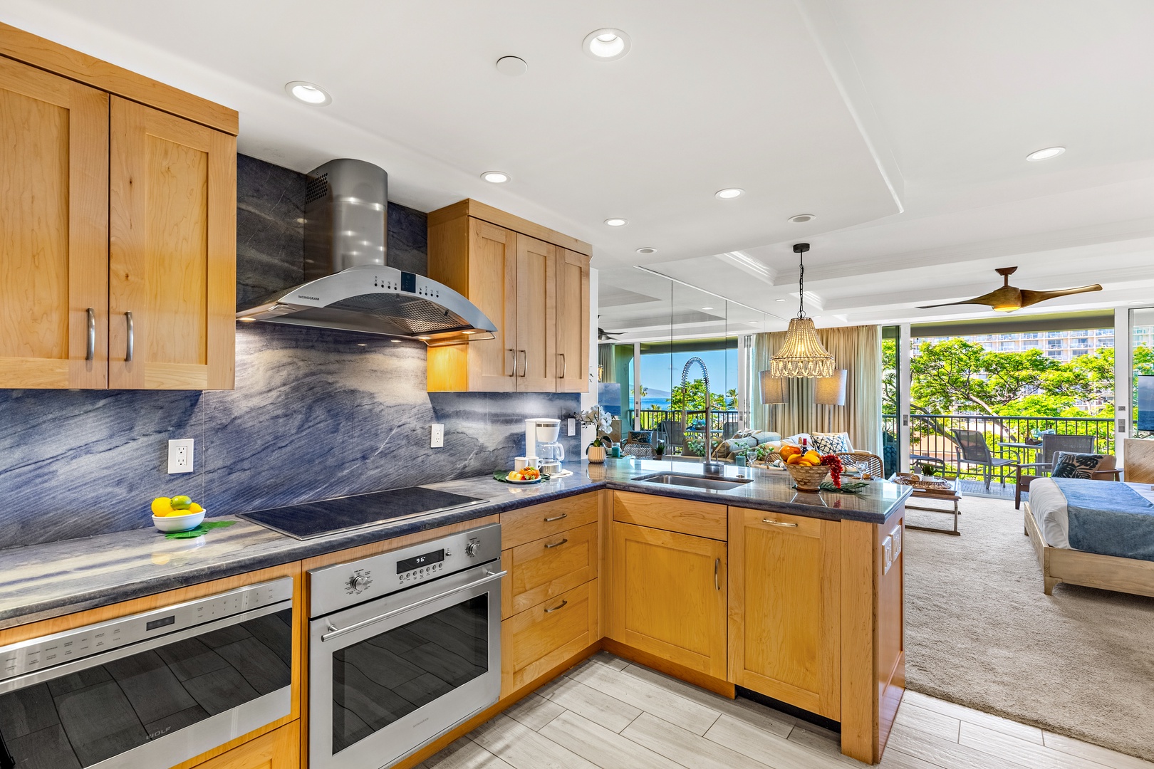 Prepare your favorite meals in this stunning kitchen featuring rich wood cabinetry, sleek stone counters, and a view that stretches across lush greenery to the sparkling ocean beyond.
