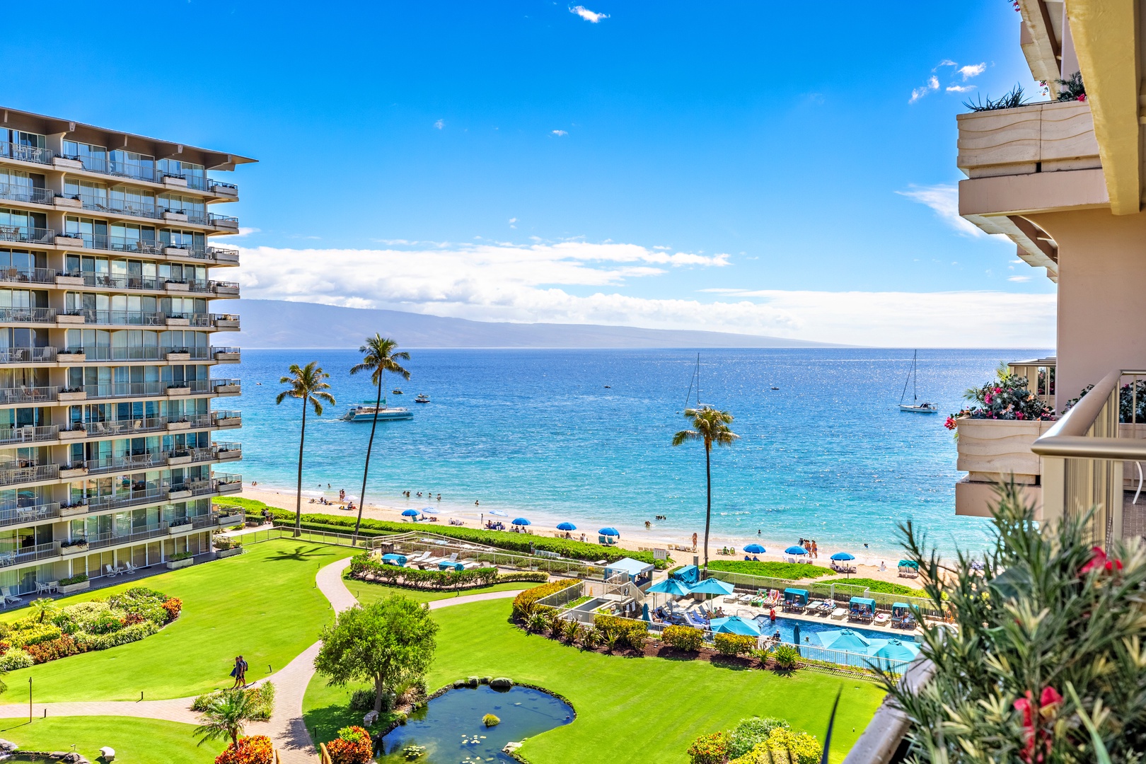 This property overlooks vibrant coastal grounds with lush lawns, a pool, and beachfront access set against the sparkling Pacific, with neighboring resort buildings framing the view.