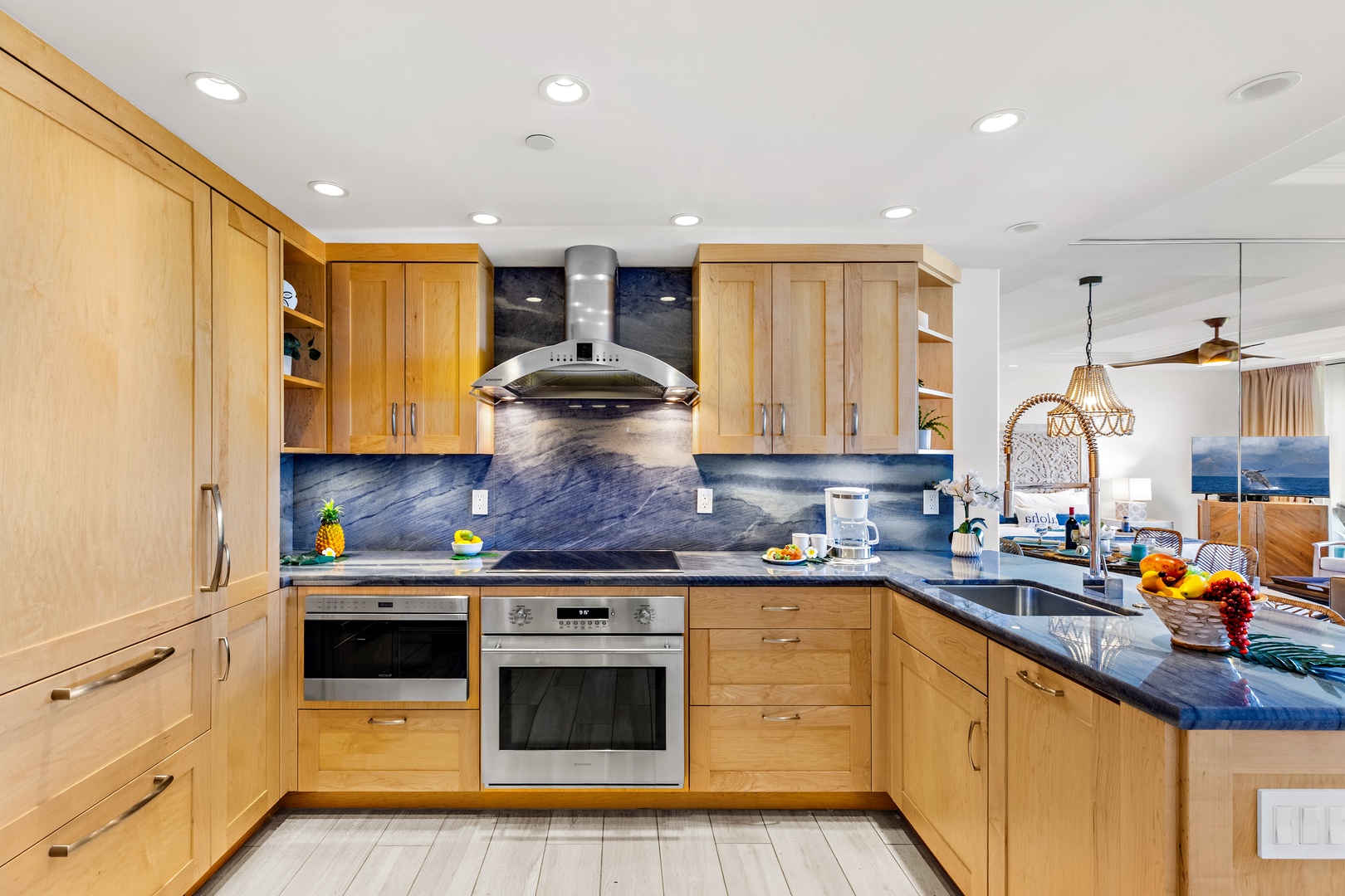 Your gourmet kitchen features beautiful wood cabinetry, premium appliances, and stunning blue granite countertops—perfect for preparing meals with an ocean view in the background.