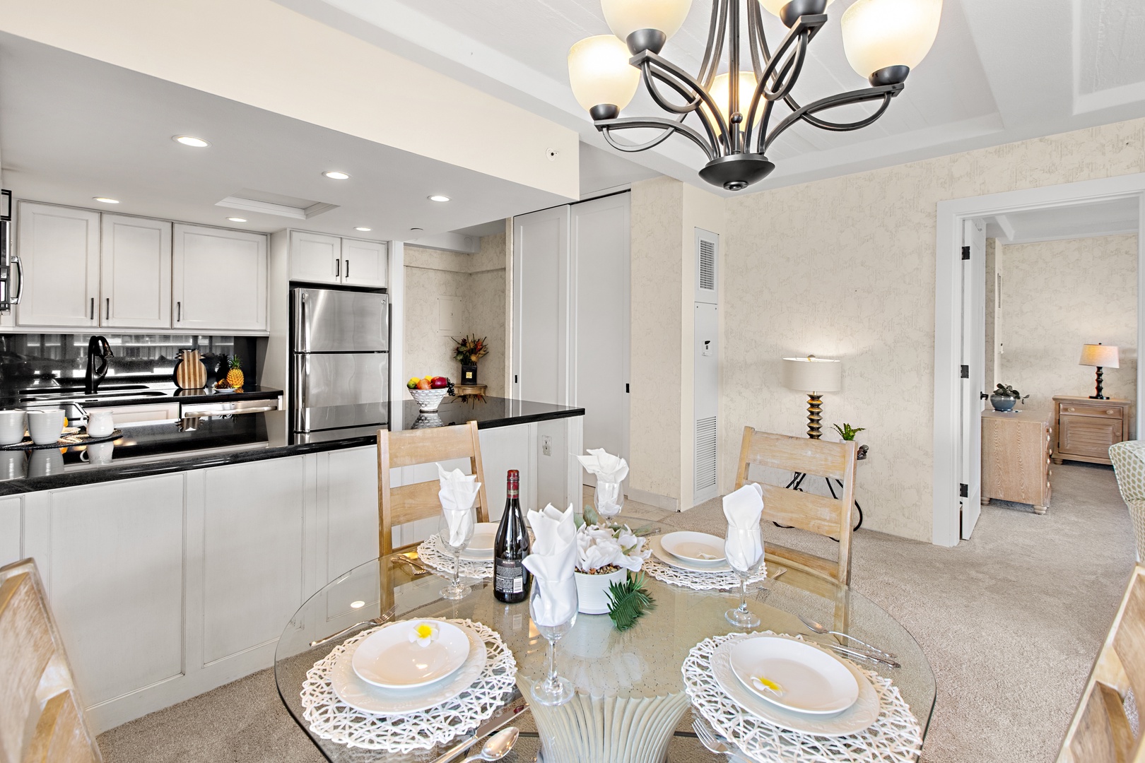 Open-concept dining and kitchen with coastal charm. Elegant table under warm chandelier light, fully equipped kitchen steps away for cooking and hosting.