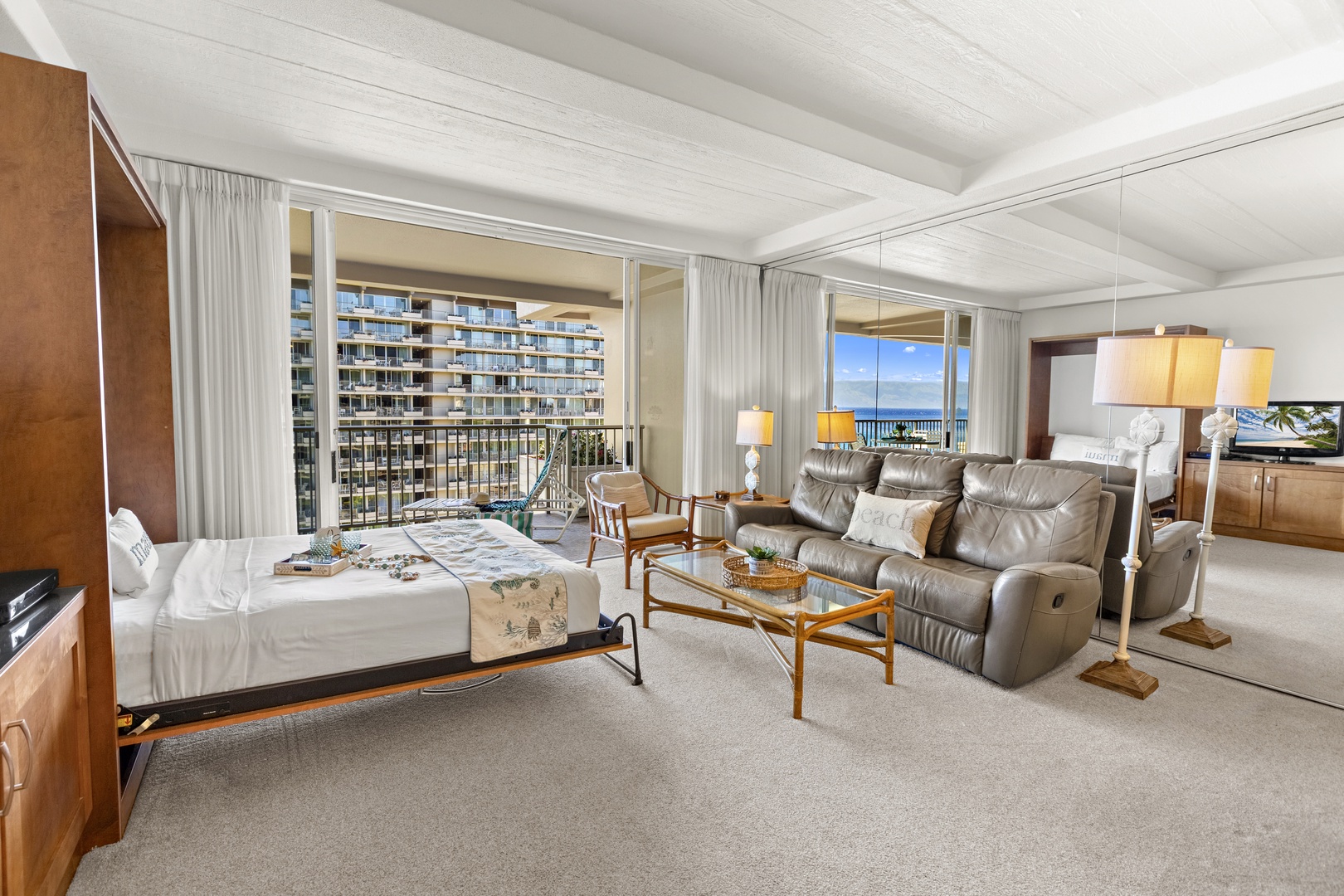 Bright, open living area featuring a plush recliner sofa, coastal-inspired furnishings, and sliding doors leading to a private lanai with ocean views.