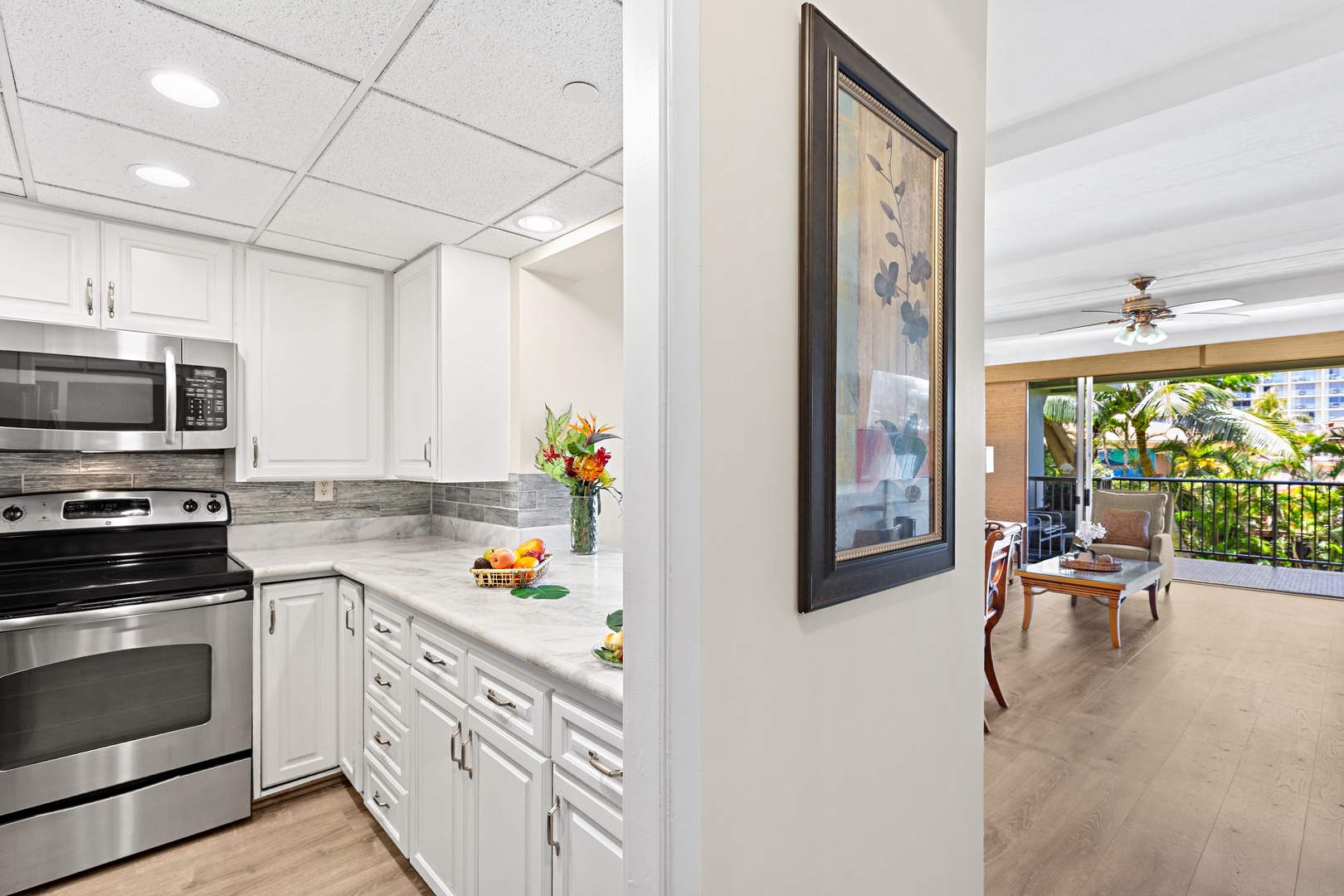Your modern kitchen with marble countertops and stainless steel appliances flows seamlessly into a bright living area with tropical balcony views, creating the perfect setting for relaxed island living.