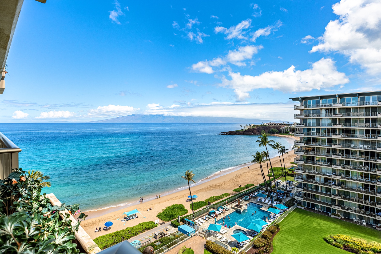 Spectacular oceanfront views showcase pristine beach, resort pools, and distant mountains from this elevated Hawaiian paradise.