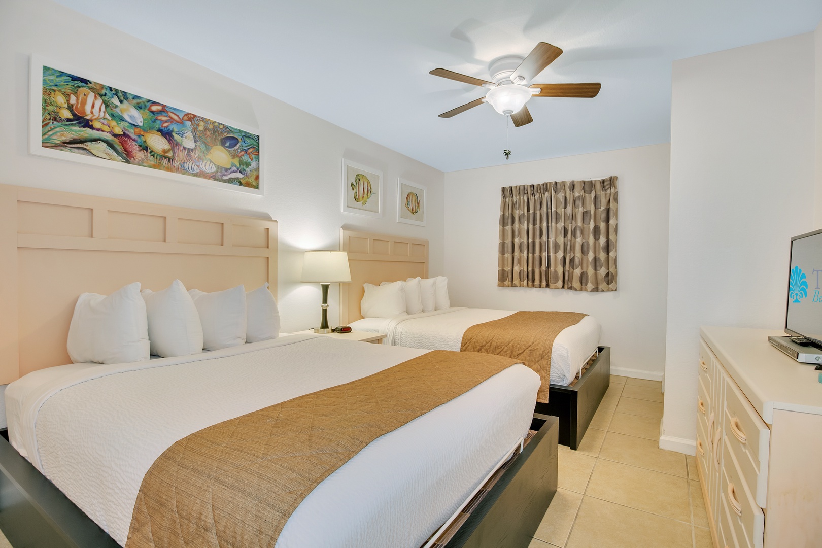Sink into crisp white linens in your bright, airy bedroom featuring twin beds, tropical artwork, and a ceiling fan for ultimate comfort.