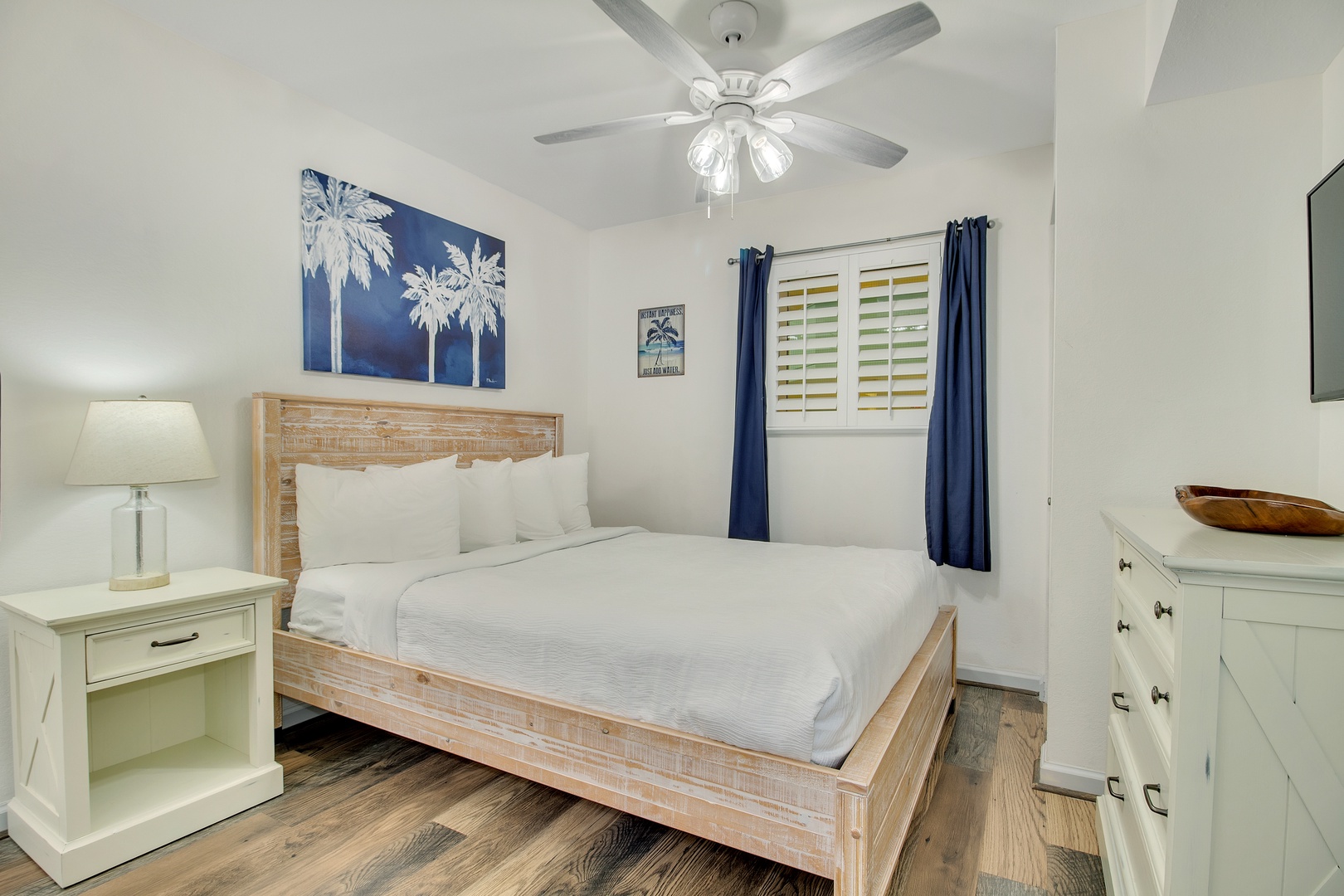 Drift off in your coastal-chic bedroom with crisp white linens, tropical artwork, and a ceiling fan for perfect comfort.