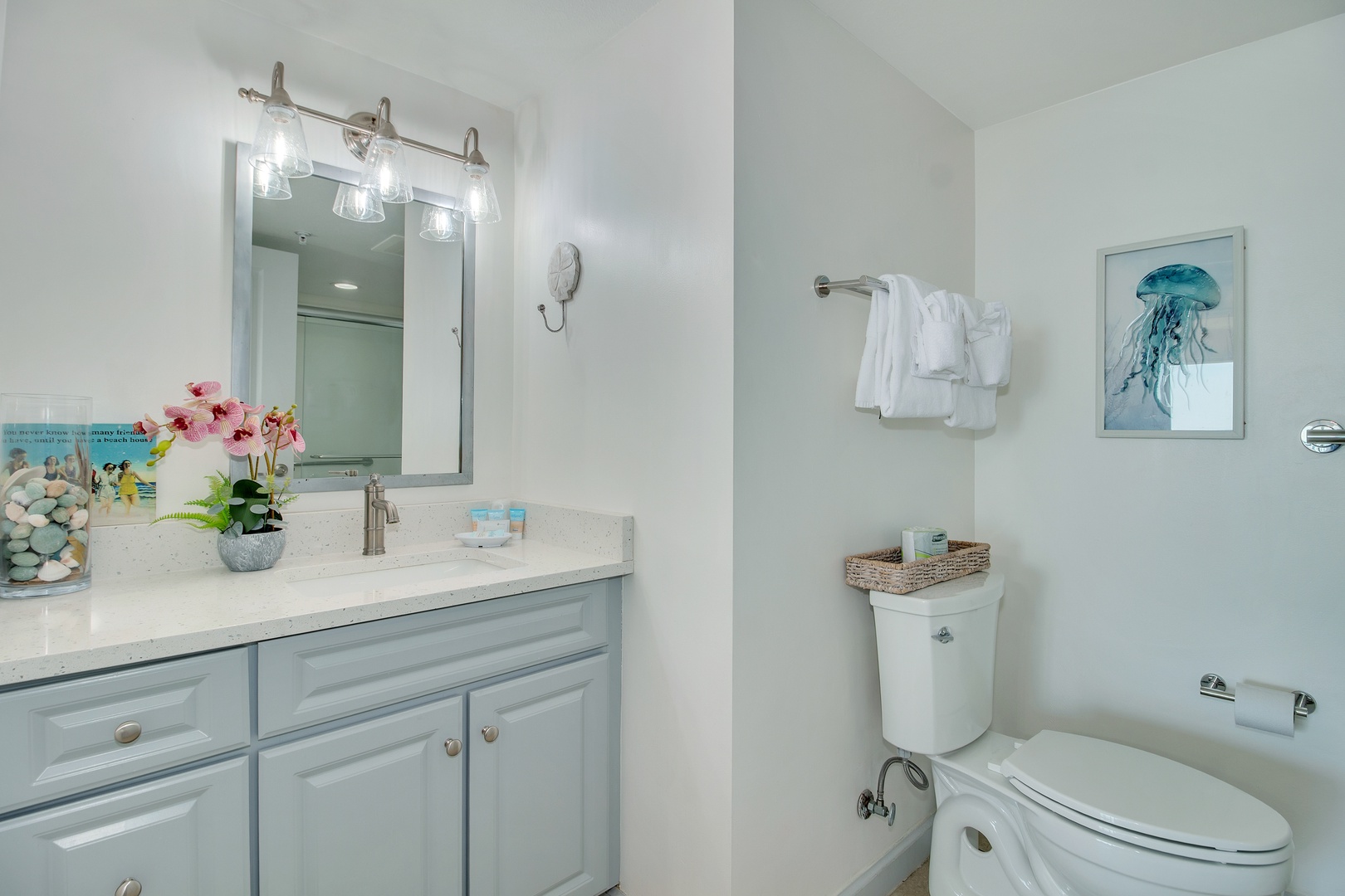 Your serene bathroom features coastal charm with soft blue vanity, fresh towels, and thoughtful touches like orchids that make you feel instantly at home.