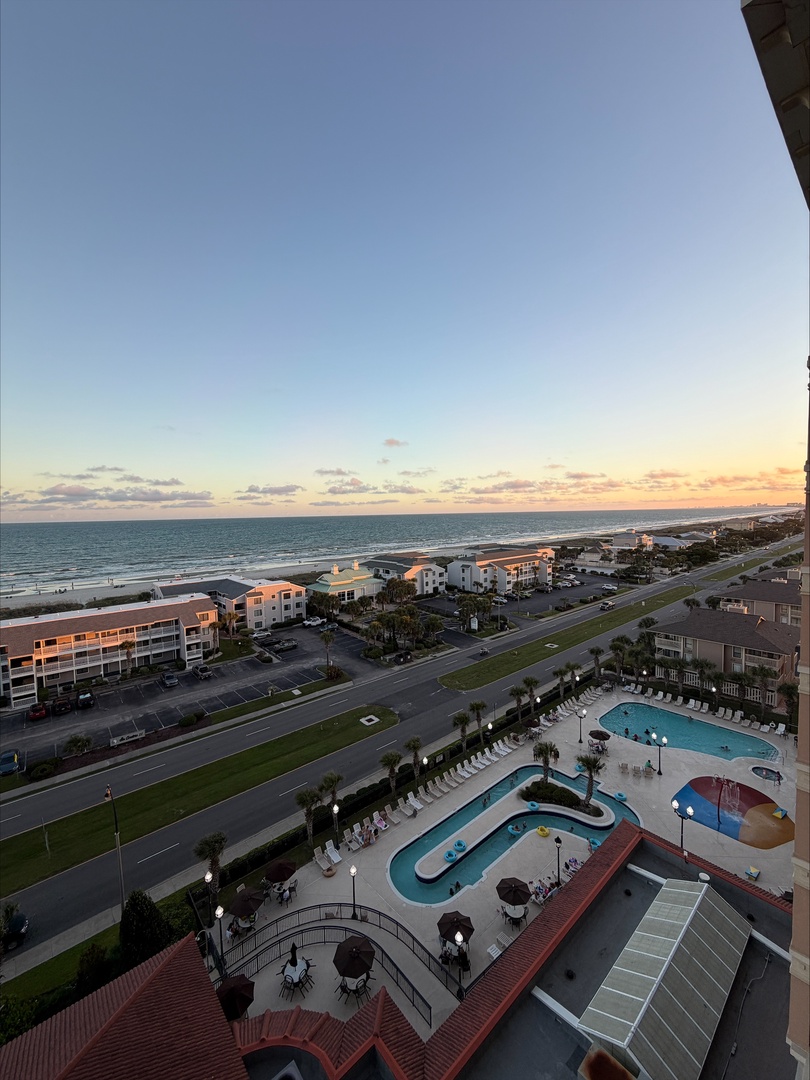 Aerial view captures the property's beachfront location, with sparkling pools, sundecks, and the ocean stretching to the horizon at sunset.