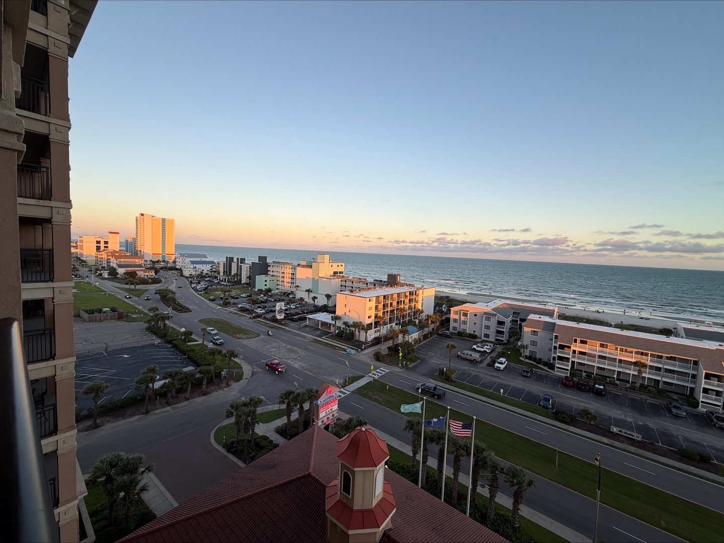 Aerial view of the beachfront area at sunset, showcasing the coastal neighborhood with ocean views and nearby buildings. The property is situated in a peaceful beachside setting with convenient access to the shore.