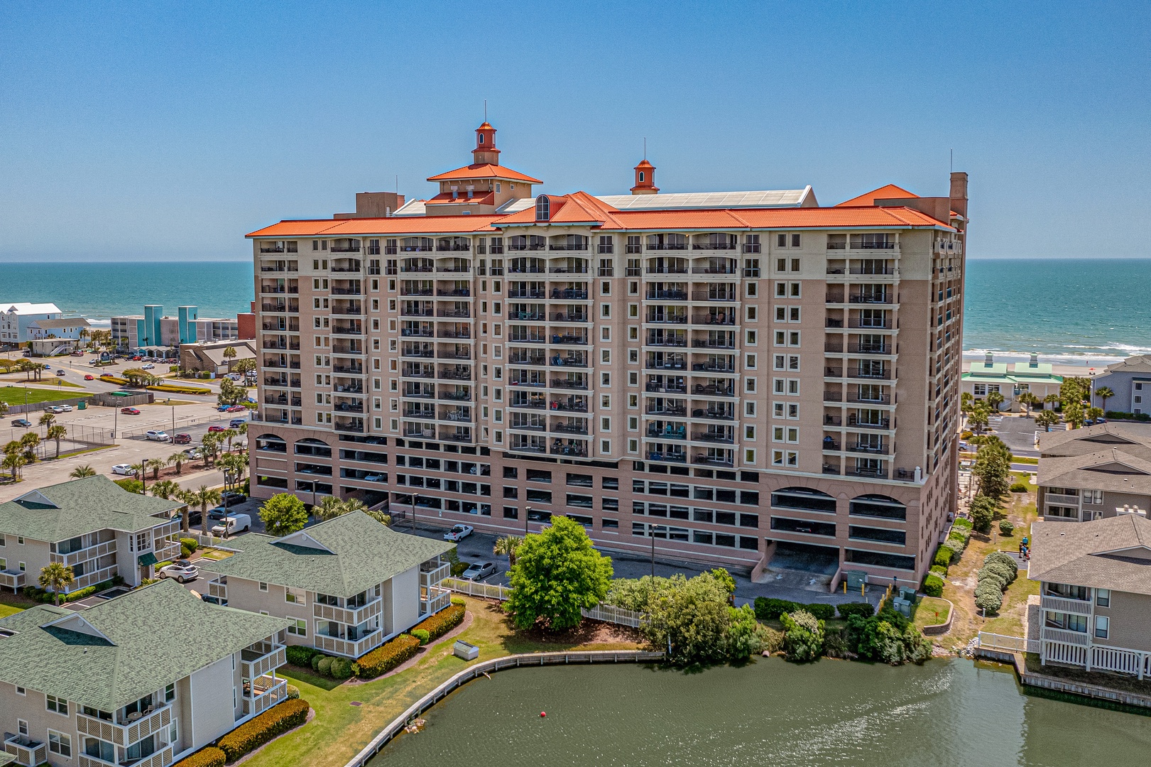Aerial view of a beachfront resort building with distinctive red-tiled towers, positioned directly on the ocean with surrounding residential properties and coastal access.