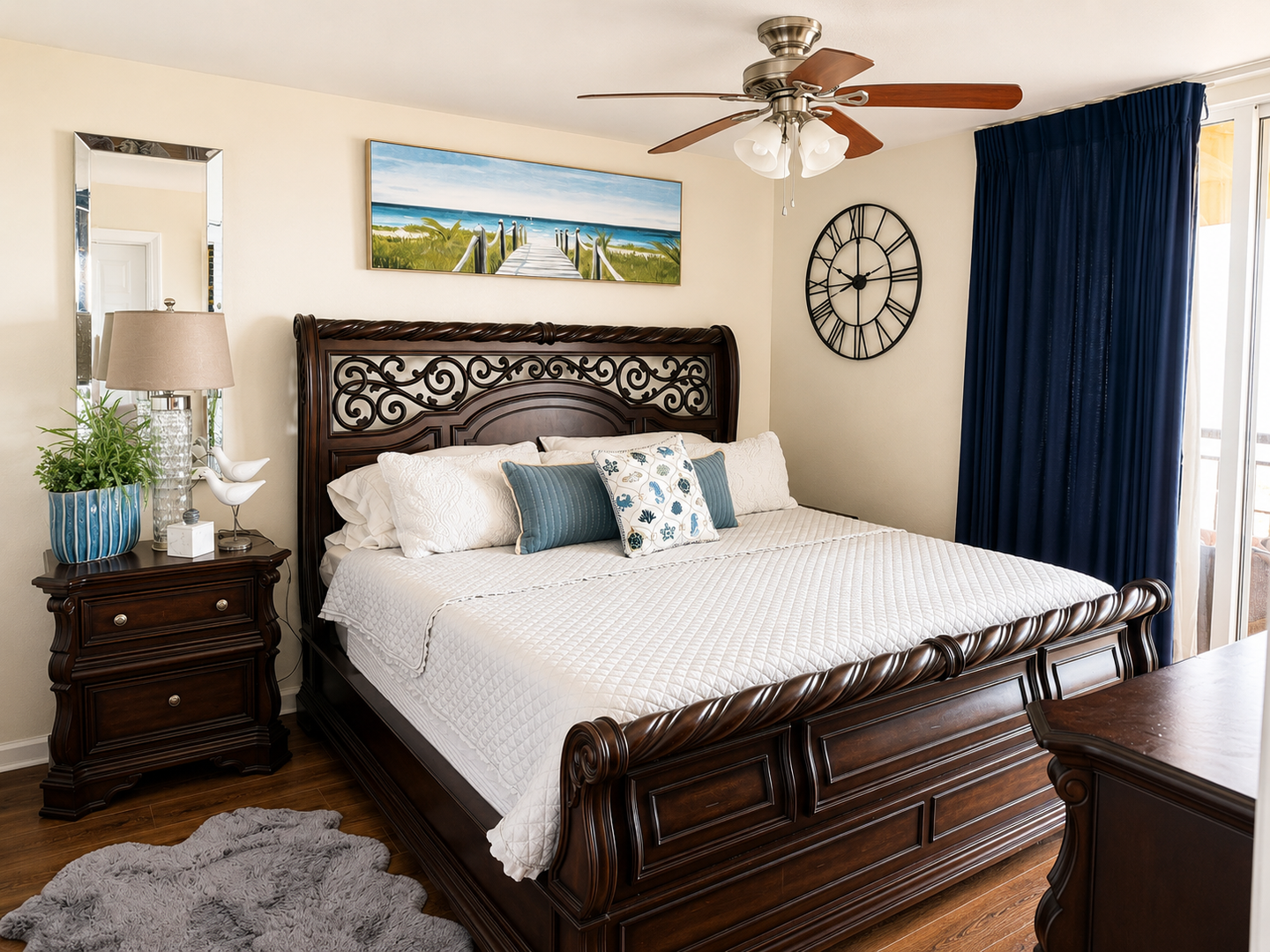 Sink into crisp white linens in this elegant bedroom, where coastal artwork above the ornate sleigh bed invites peaceful dreams and the gentle whir of the ceiling fan promises cool comfort.