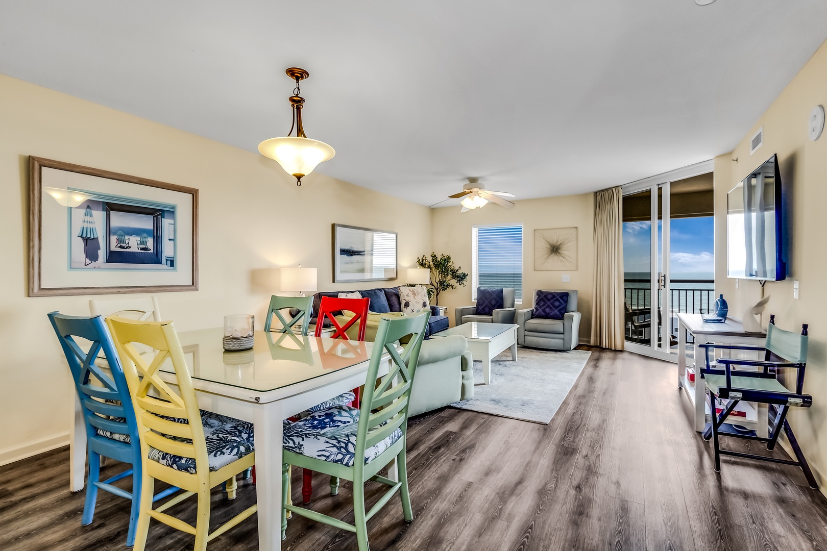 Your bright, cheerful living space combines comfort with coastal charm, featuring colorful dining chairs and ocean views from your private balcony.