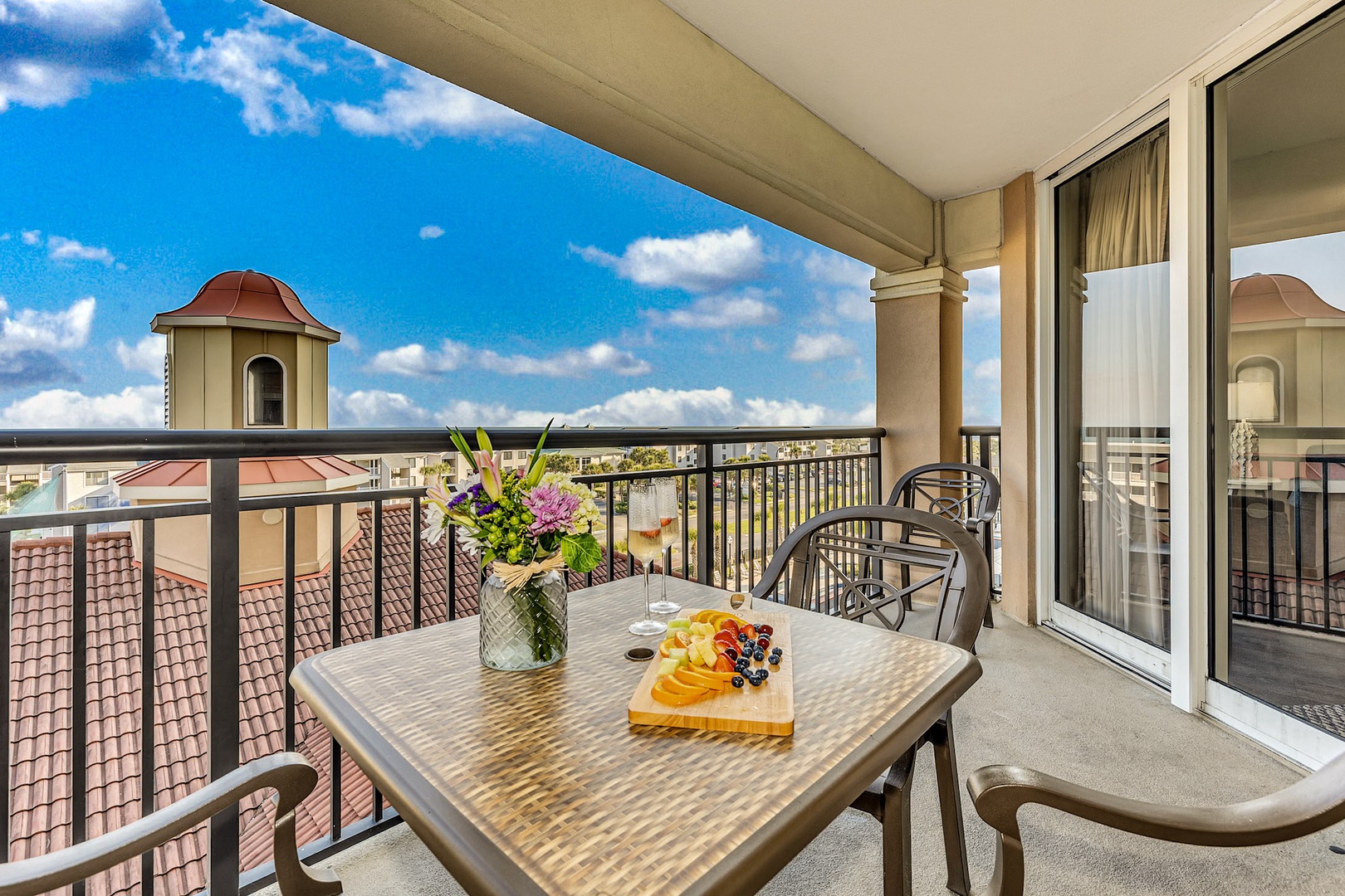 Your private balcony invites leisurely mornings with fresh flowers and sweeping views over charming rooftops under bright, open skies.