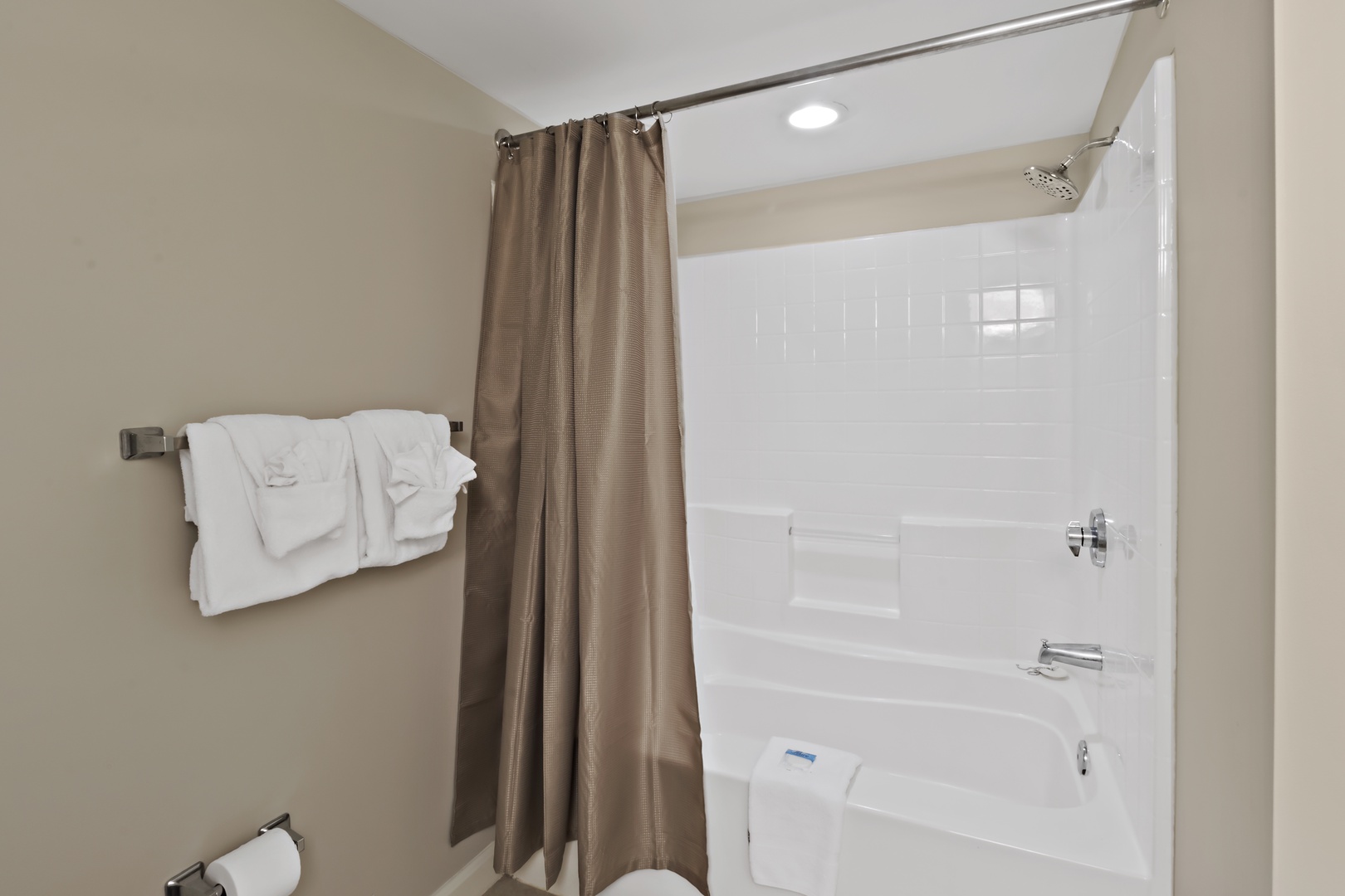 Step into your spotless bathroom with a refreshing tub-shower combo and fluffy white towels waiting for your relaxation.