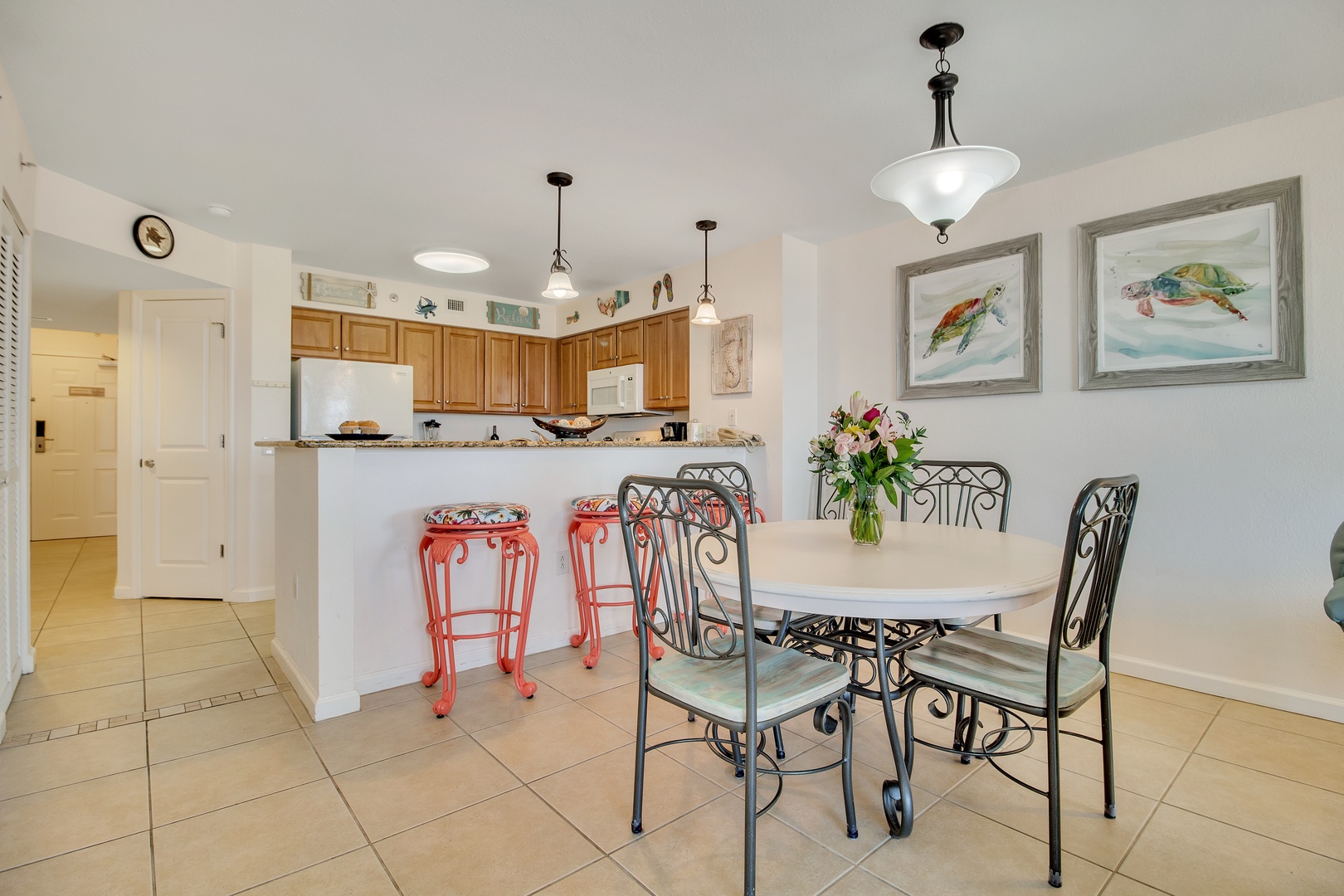 Your open kitchen flows into a bright dining area where colorful stools and coastal art create a cheerful gathering space for shared meals.