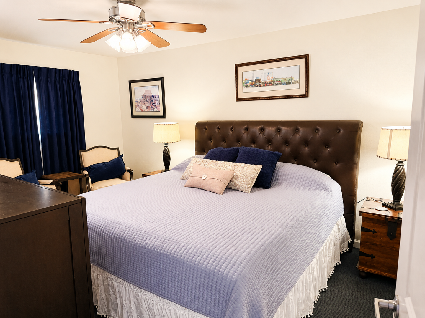 Your bedroom features a plush tufted headboard, soft linens, and ambient lighting from bedside lamps. The ceiling fan keeps you comfortable year-round.