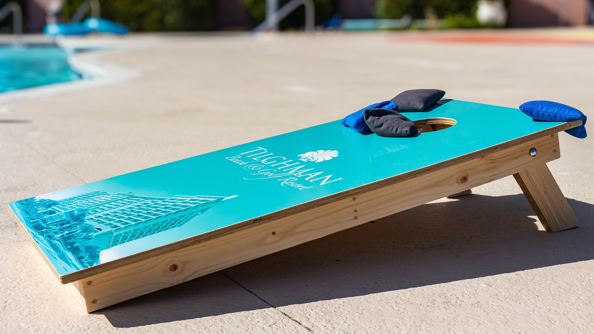A cornhole board set stands ready by the pool, inviting you to enjoy a friendly outdoor game under the sun during your stay.