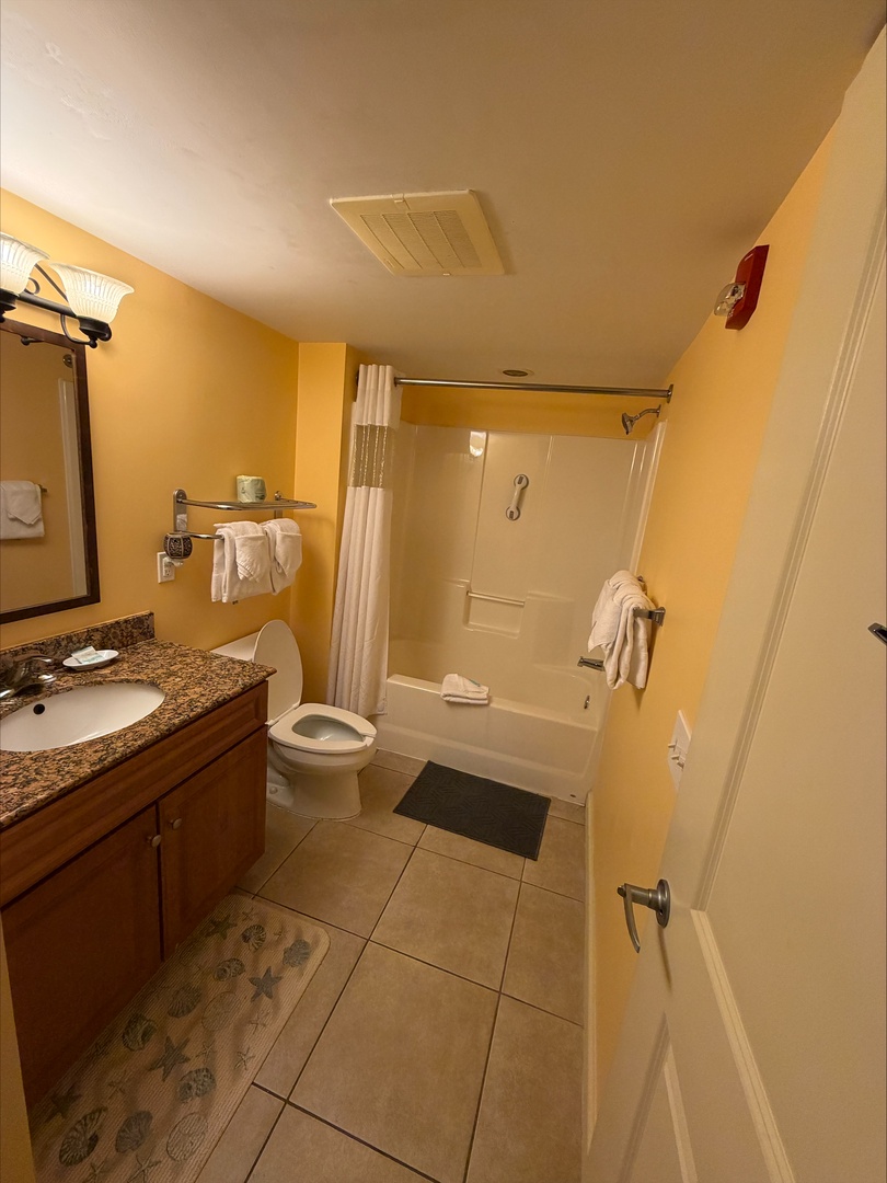 Your private bathroom features warm golden tones, a granite vanity, and a full tub-shower combo with fresh towels ready for you.