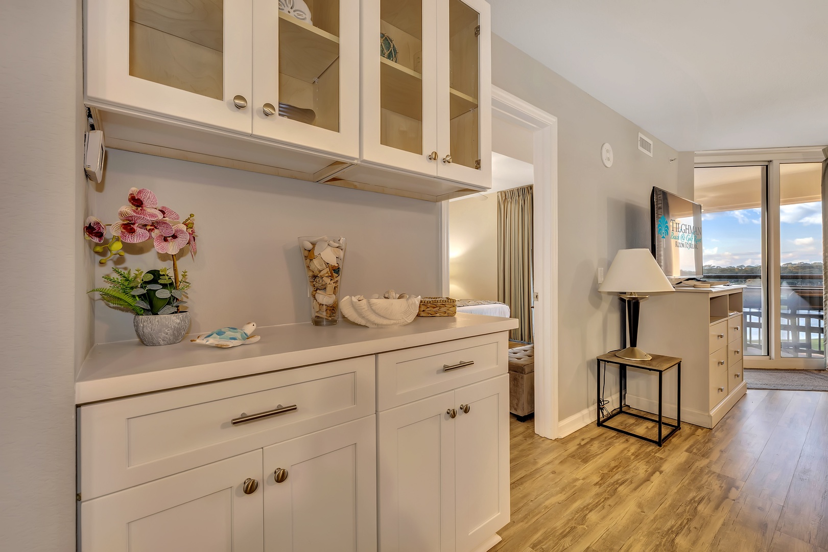 Step into your bright, coastal retreat where elegant built-in storage and warm wood floors guide you toward stunning water views just beyond the balcony doors.