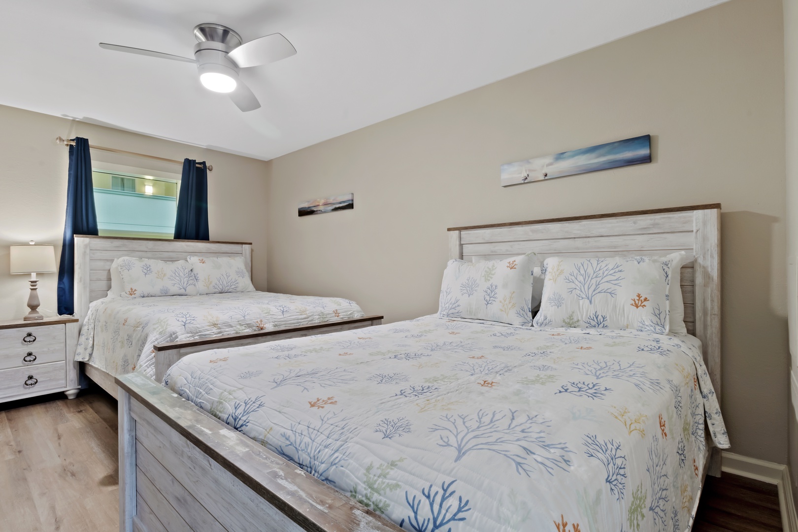 Drift off to sleep in this tranquil bedroom with two comfortable beds, soft coral-patterned linens, and a gentle ceiling fan overhead.