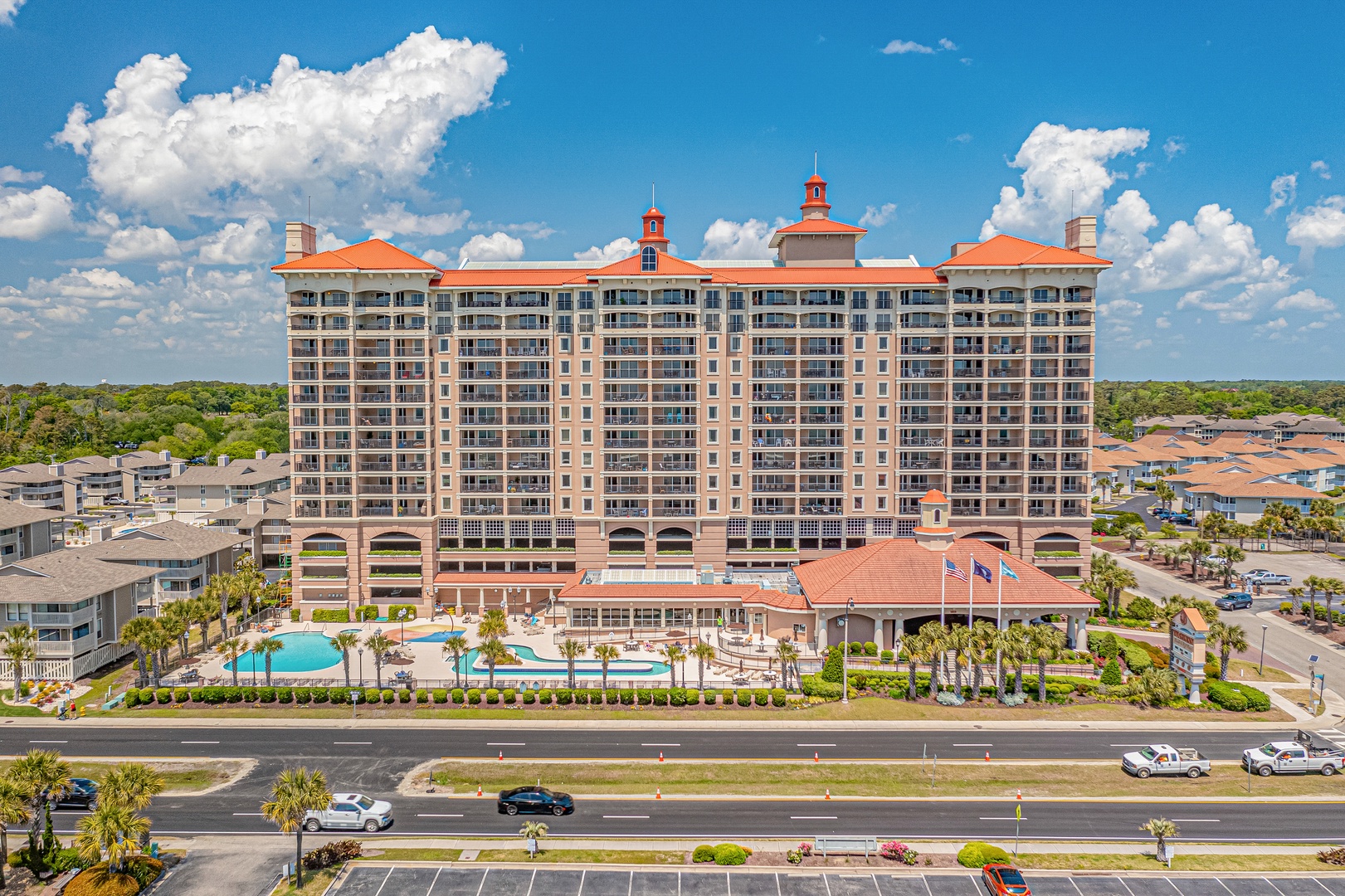 A distinctive resort building with Mediterranean-style architecture features terracotta roofs and twin bell towers. Multiple pools and palm-lined grounds create an inviting tropical setting near the entrance.