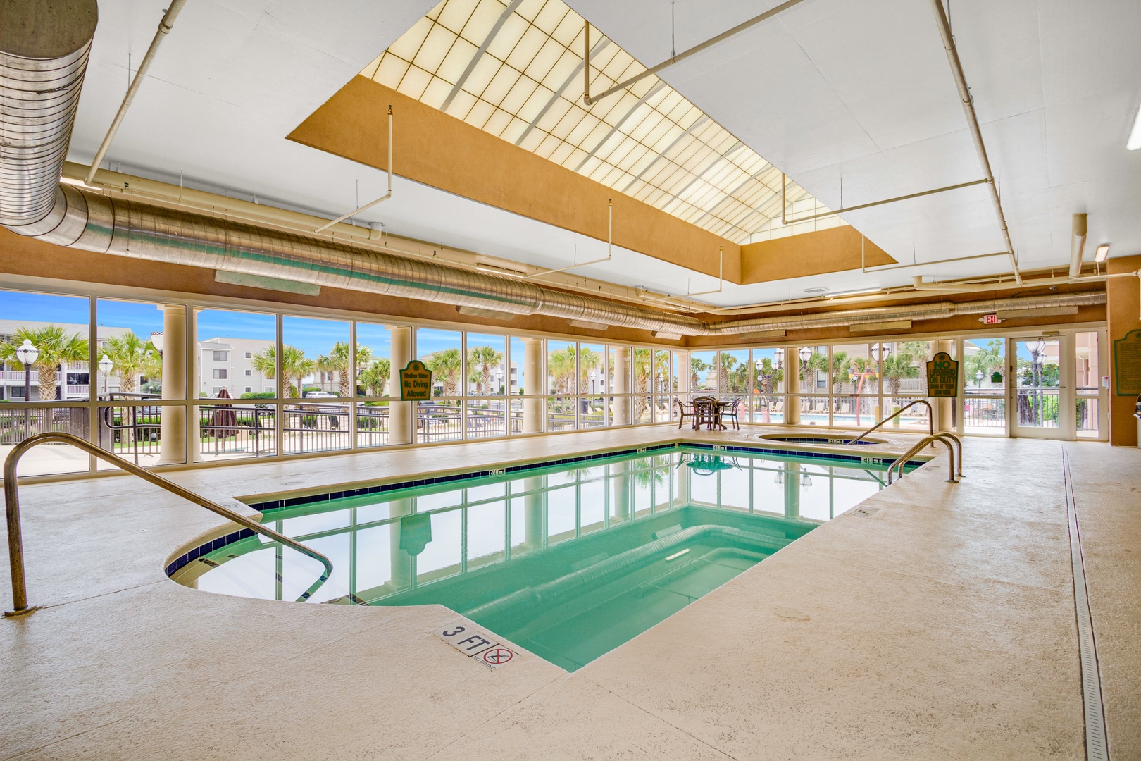 Indoor pool area with bright sunshine and views overlooking palms and pool decks outside, inviting you to swim in comfort year-round.