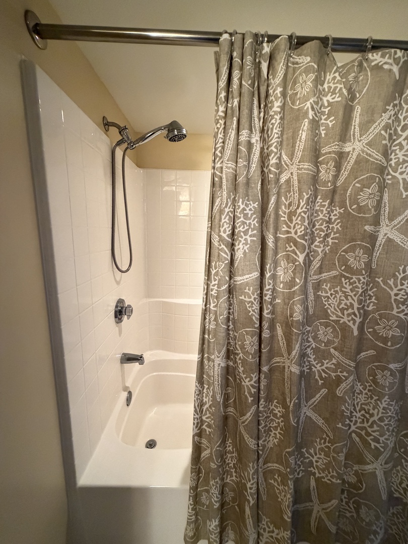 Unwind in your spacious soaking tub with handheld shower, where coastal-themed window treatments filter natural light for your peaceful bathing retreat.