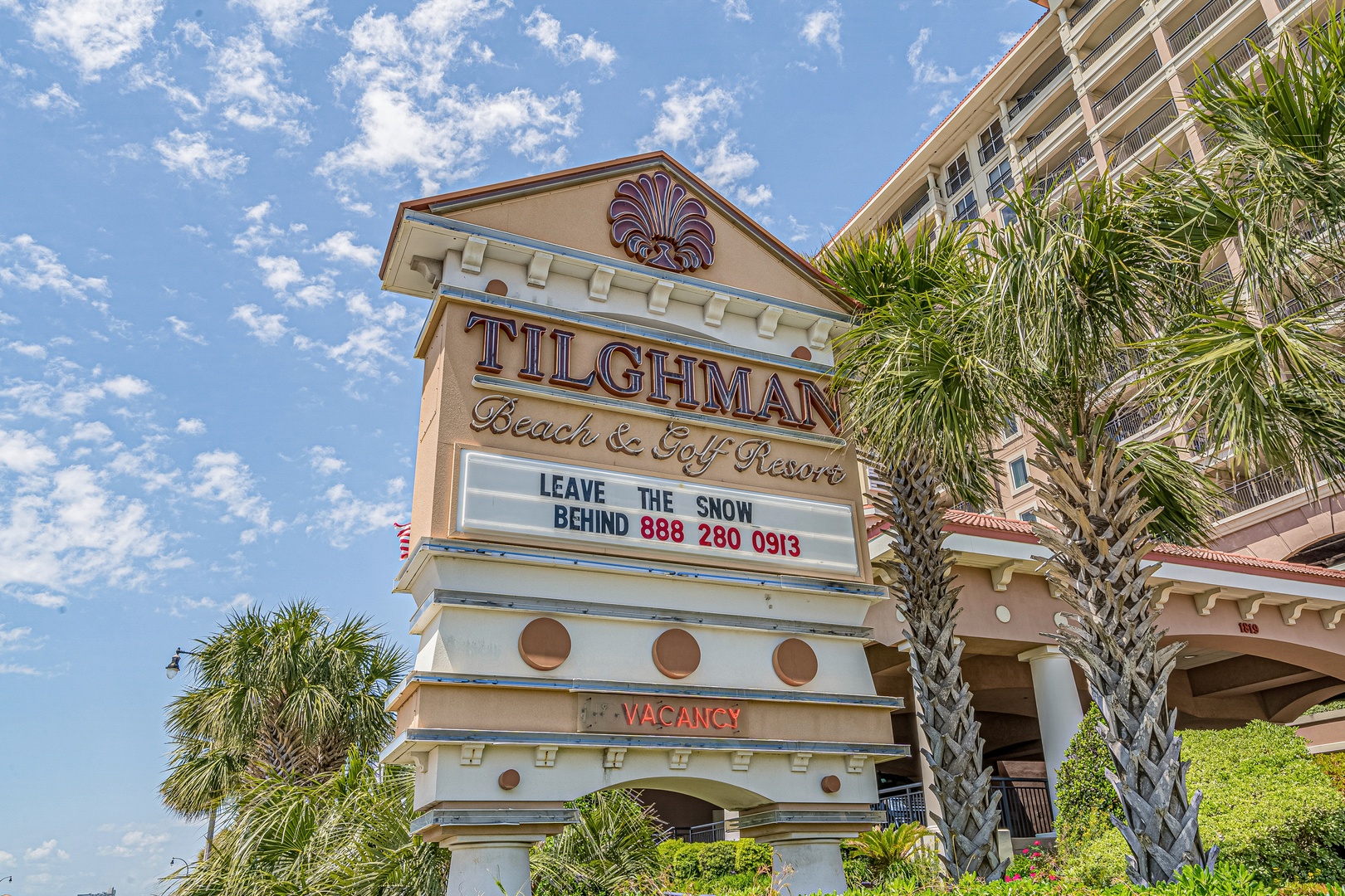The Tilghman Beach & Golf Resort entrance sign welcomes visitors to a coastal destination with palm trees and sunny skies framing the property's distinctive signage.