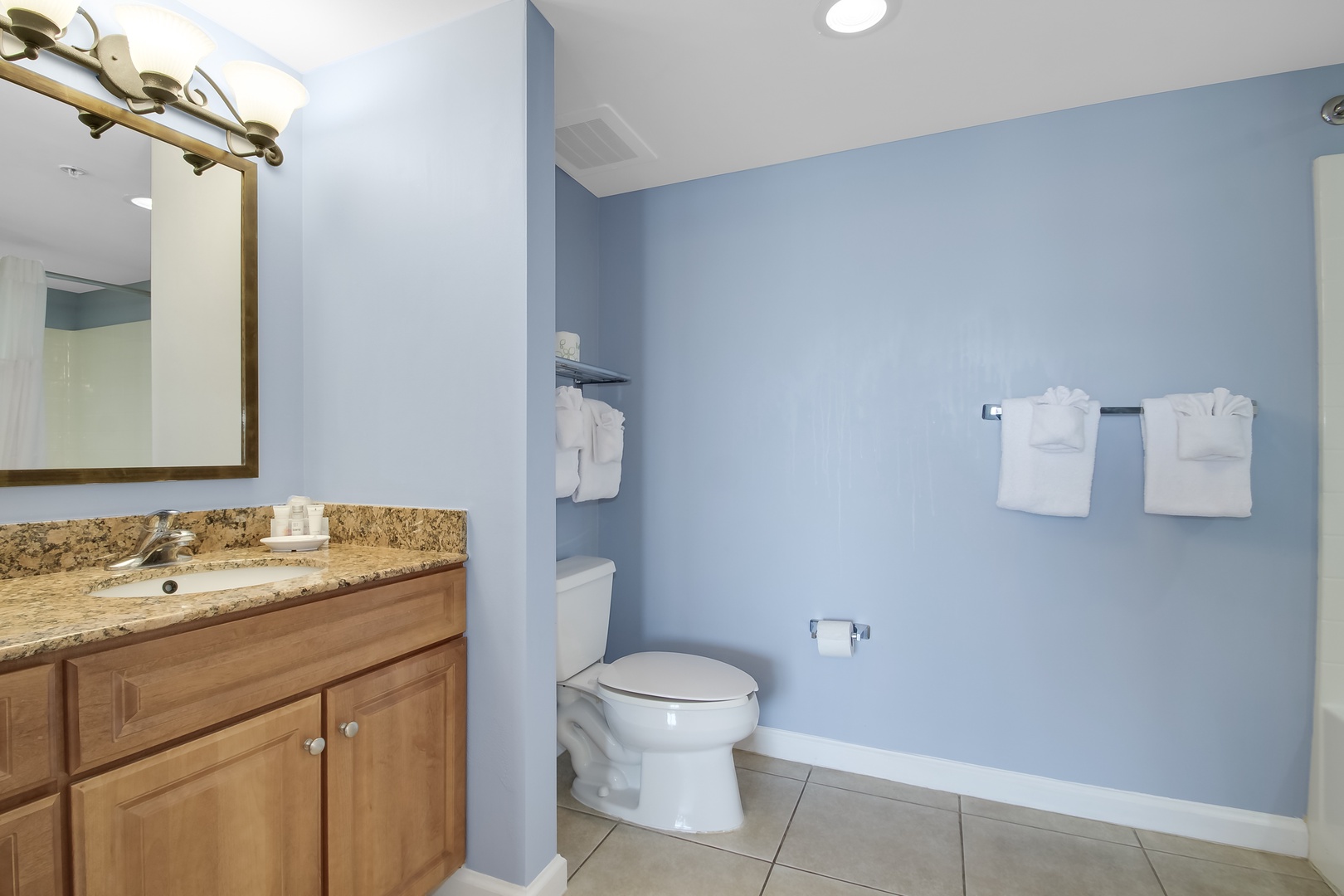 Refresh in your spacious bathroom featuring granite countertops, wooden vanity, and soothing blue walls with fluffy white towels awaiting.
