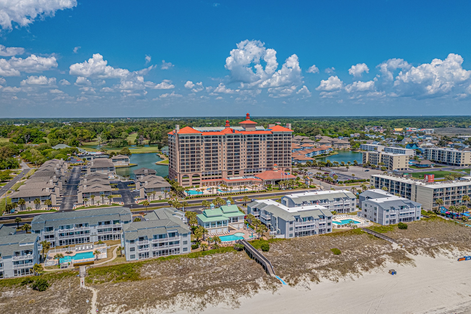 Aerial view of a beachfront resort community with multiple properties, pools, and direct beach access along a scenic waterfront neighborhood.