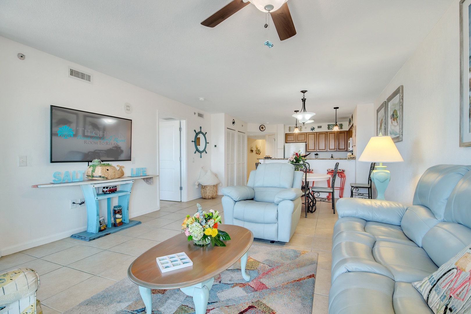 Relax in your bright, coastal-themed living space with comfortable seating, modern TV, and open kitchen perfect for vacation meals.