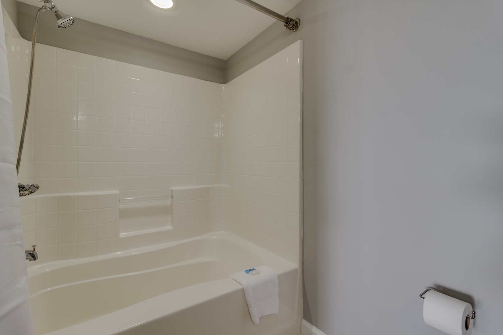 Unwind in your private bathroom featuring a pristine tub-shower combo with gleaming white tile and modern fixtures for ultimate relaxation.