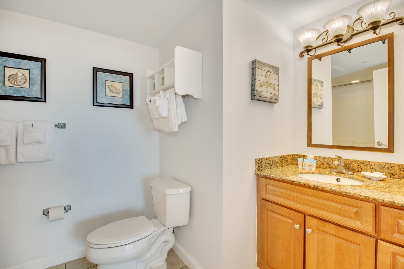 Freshen up in your private bathroom featuring granite countertops, warm wood cabinetry, and coastal-themed artwork that sets a relaxing tone.