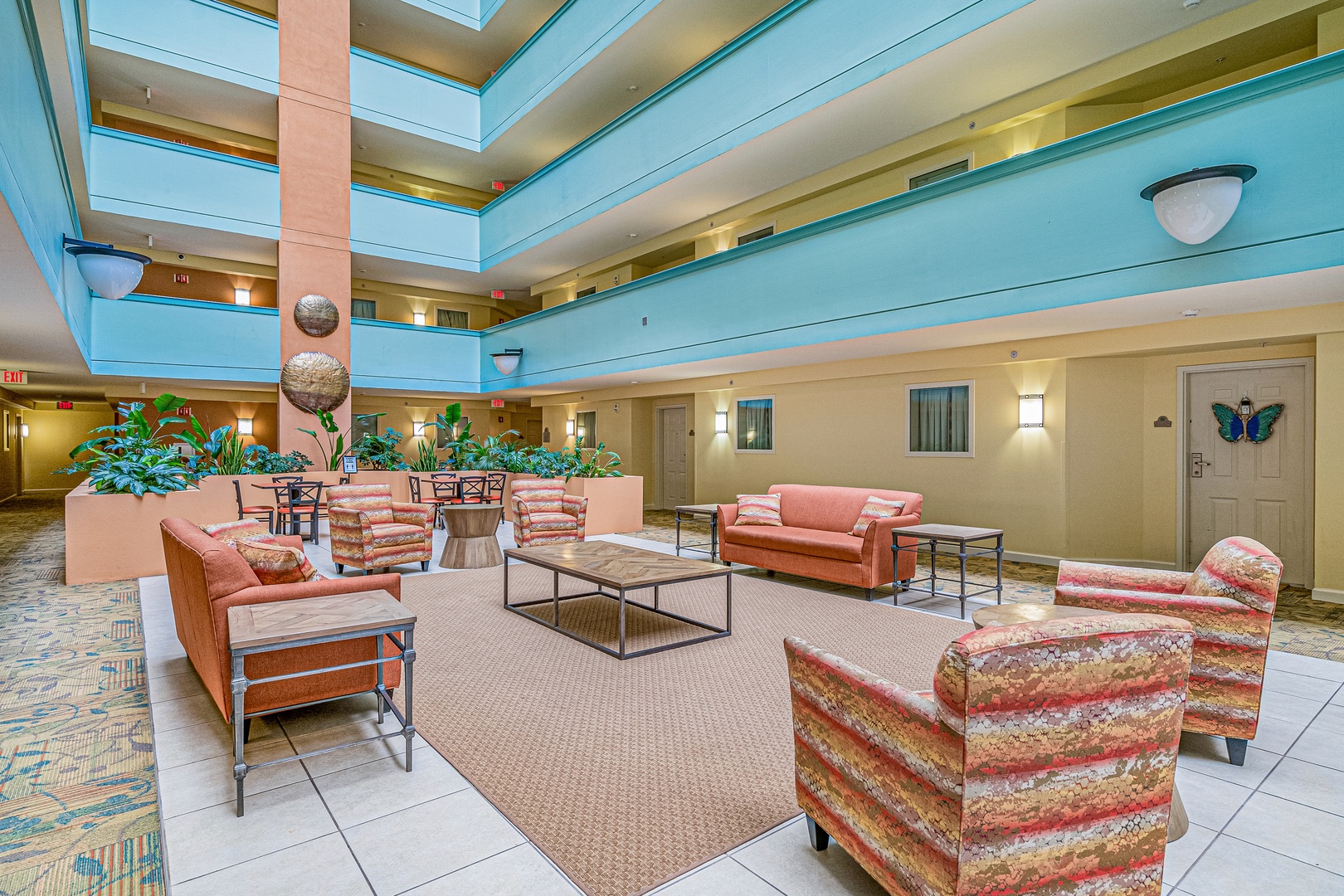A bright, airy atrium featuring warm coral seating, lush greenery, and natural light streaming through skylights creates a welcoming space to gather and unwind.