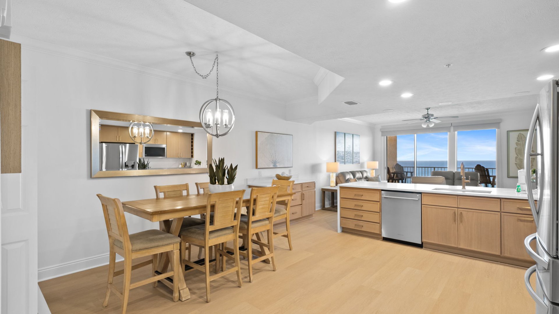 Your bright, open kitchen flows seamlessly into the dining area, featuring warm wood finishes and stunning ocean views through floor-to-ceiling windows.