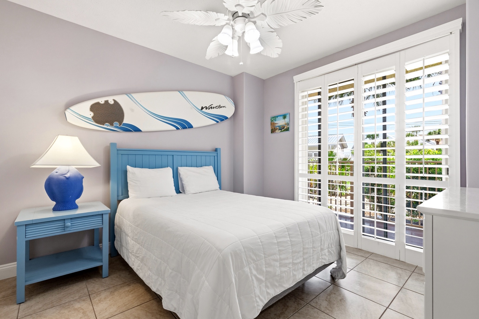 Rest peacefully in your coastal-themed bedroom with tropical ceiling fan, unique surfboard art, and French doors opening to outdoor views.