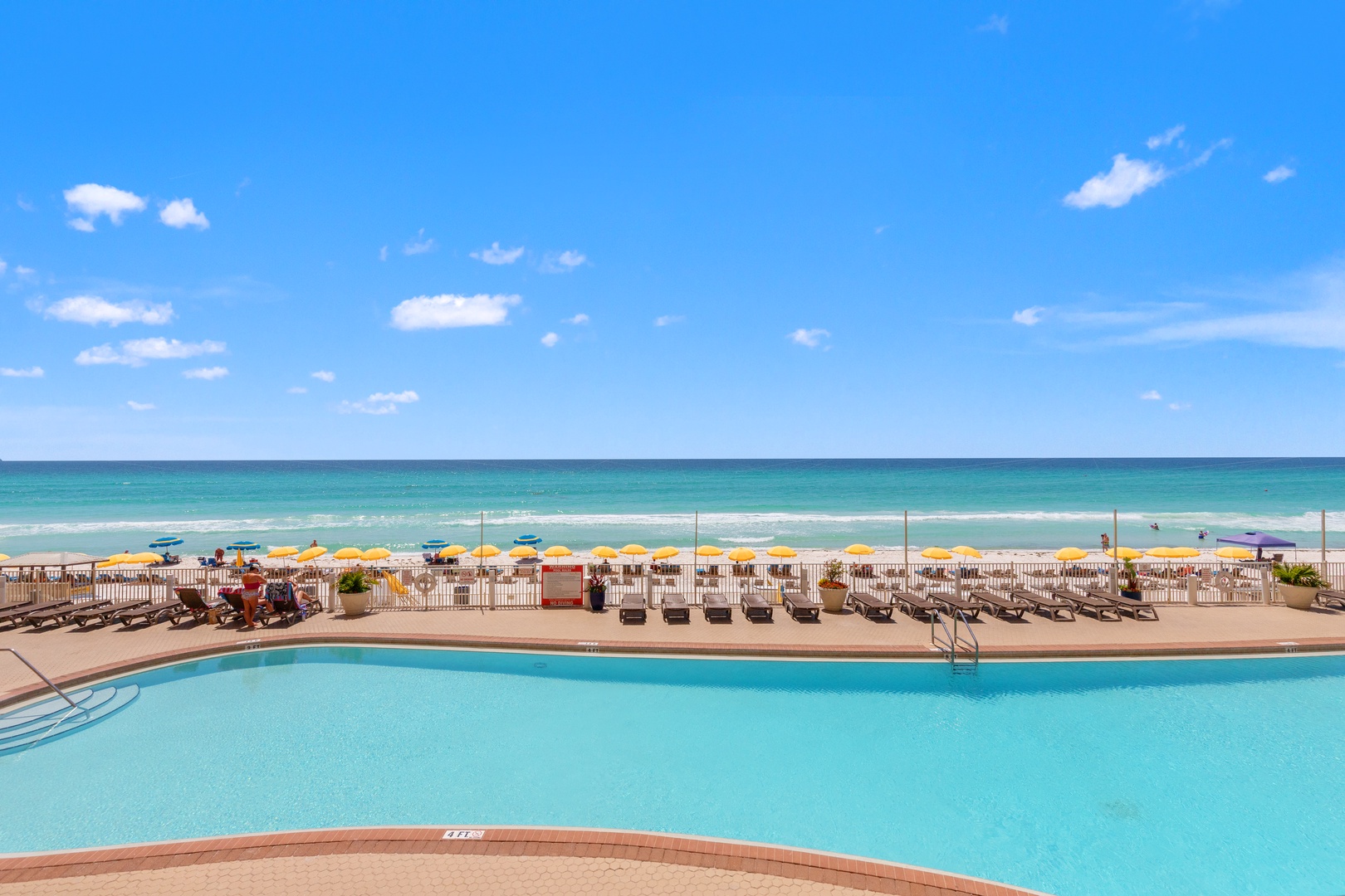 Sparkling pool deck overlooking pristine beach with colorful umbrellas and crystal-clear waters stretching to the horizon.