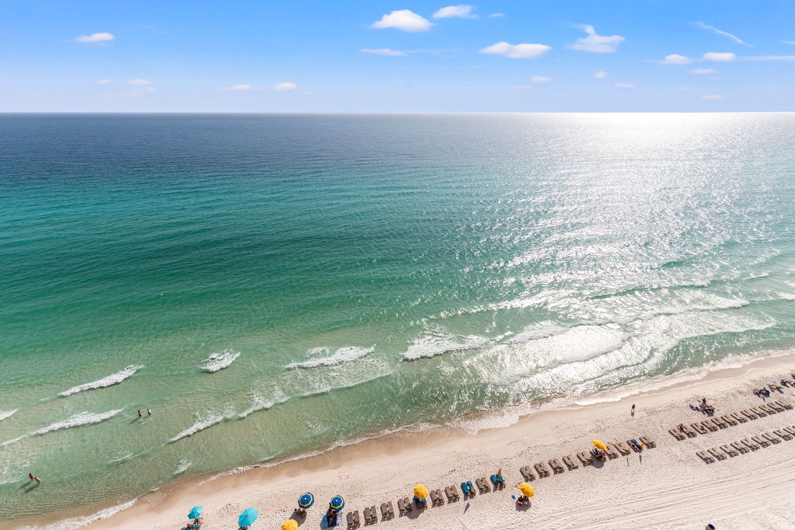 The property features beachfront access with pristine emerald-green waters, soft white sands, and organized lounge seating along the shoreline.