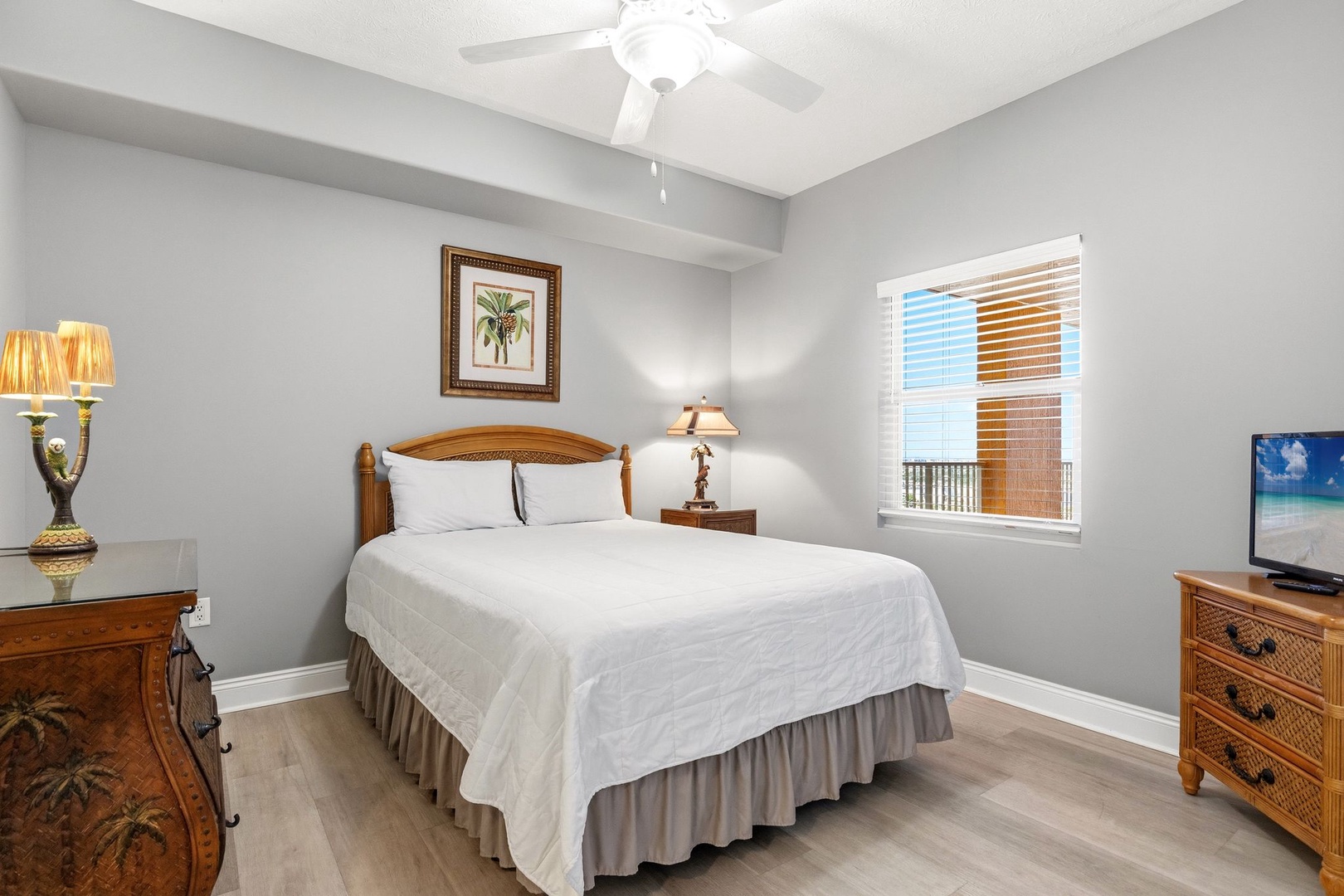 Sink into crisp white linens in your peaceful bedroom, where warm wood furnishings and tropical artwork create the perfect retreat for restful nights.