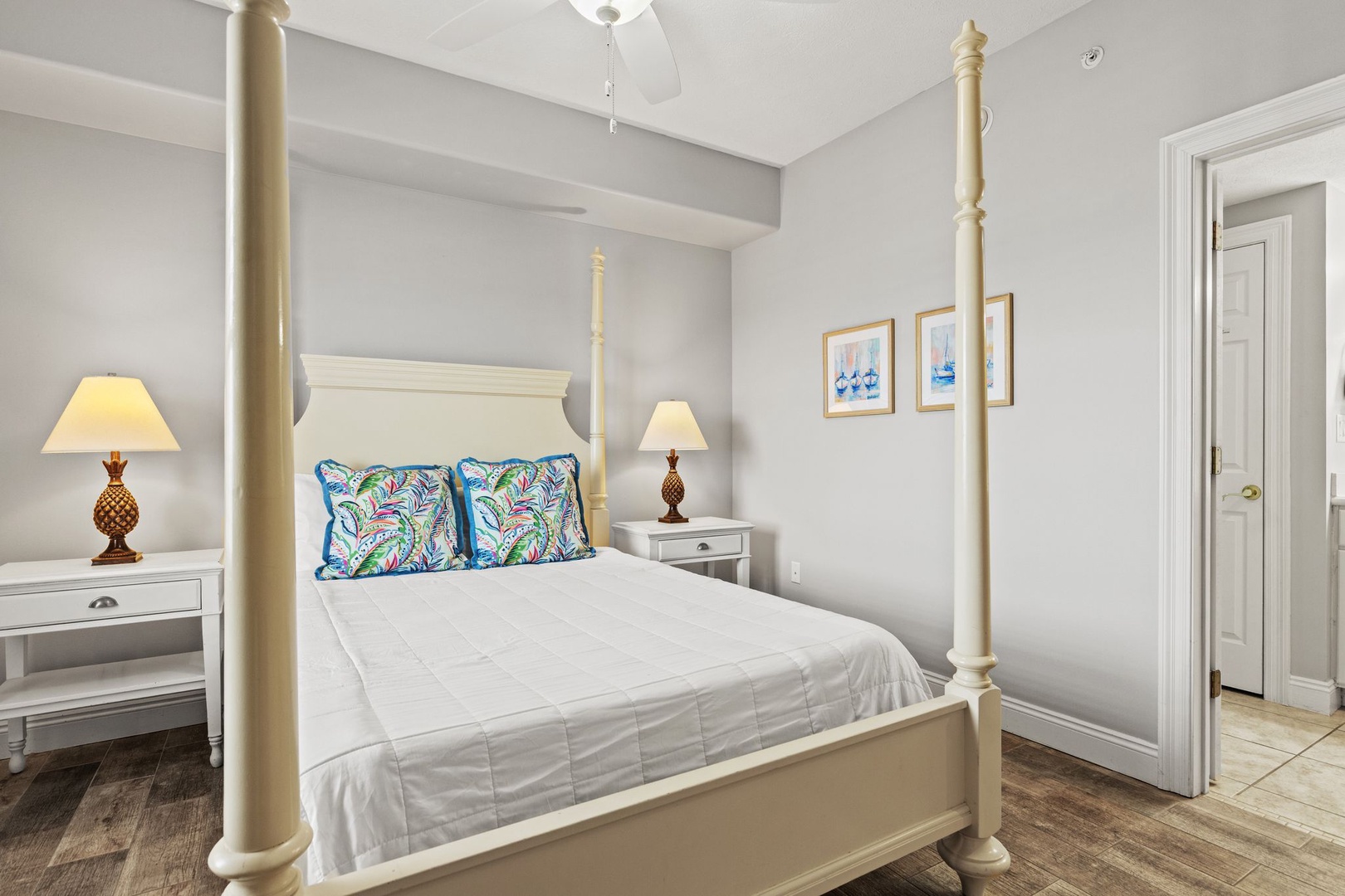 Unwind in your restful bedroom, featuring a stately four-poster bed with plush linens, warm bedside lighting, and coastal artwork that sets a tranquil, beachy mood.