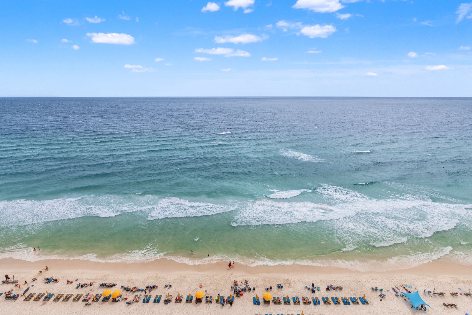 Aerial view of pristine beachfront with turquoise Gulf waters and sugar-white sand, featuring convenient beach chair rentals and easy access to the shoreline.