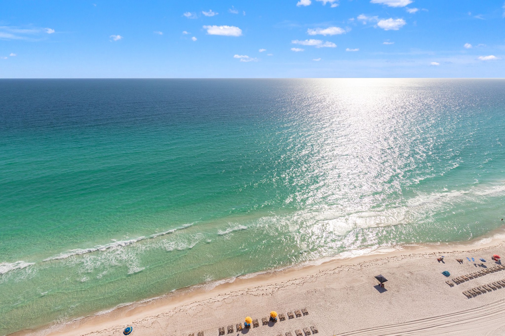 Stunning aerial perspective of pristine turquoise waters meeting golden sand, with beachgoers enjoying the perfect coastline setting.