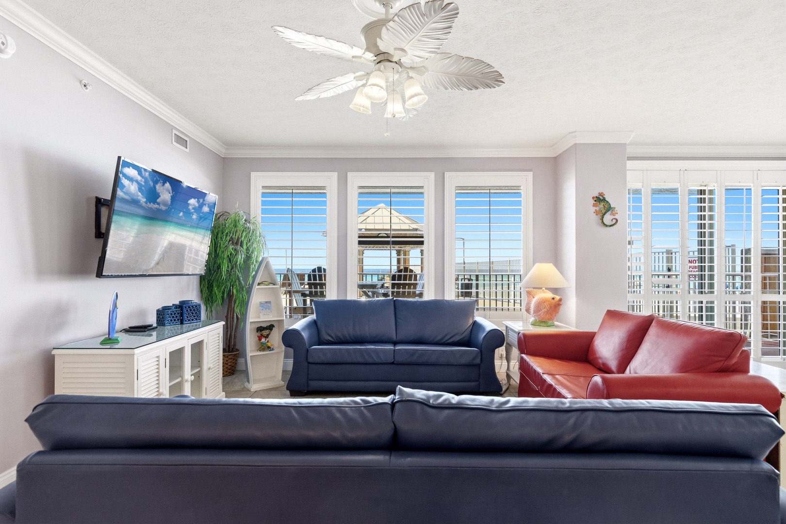Unwind in your spacious living room with plush leather seating, tropical ceiling fan, and stunning city views through floor-to-ceiling windows.