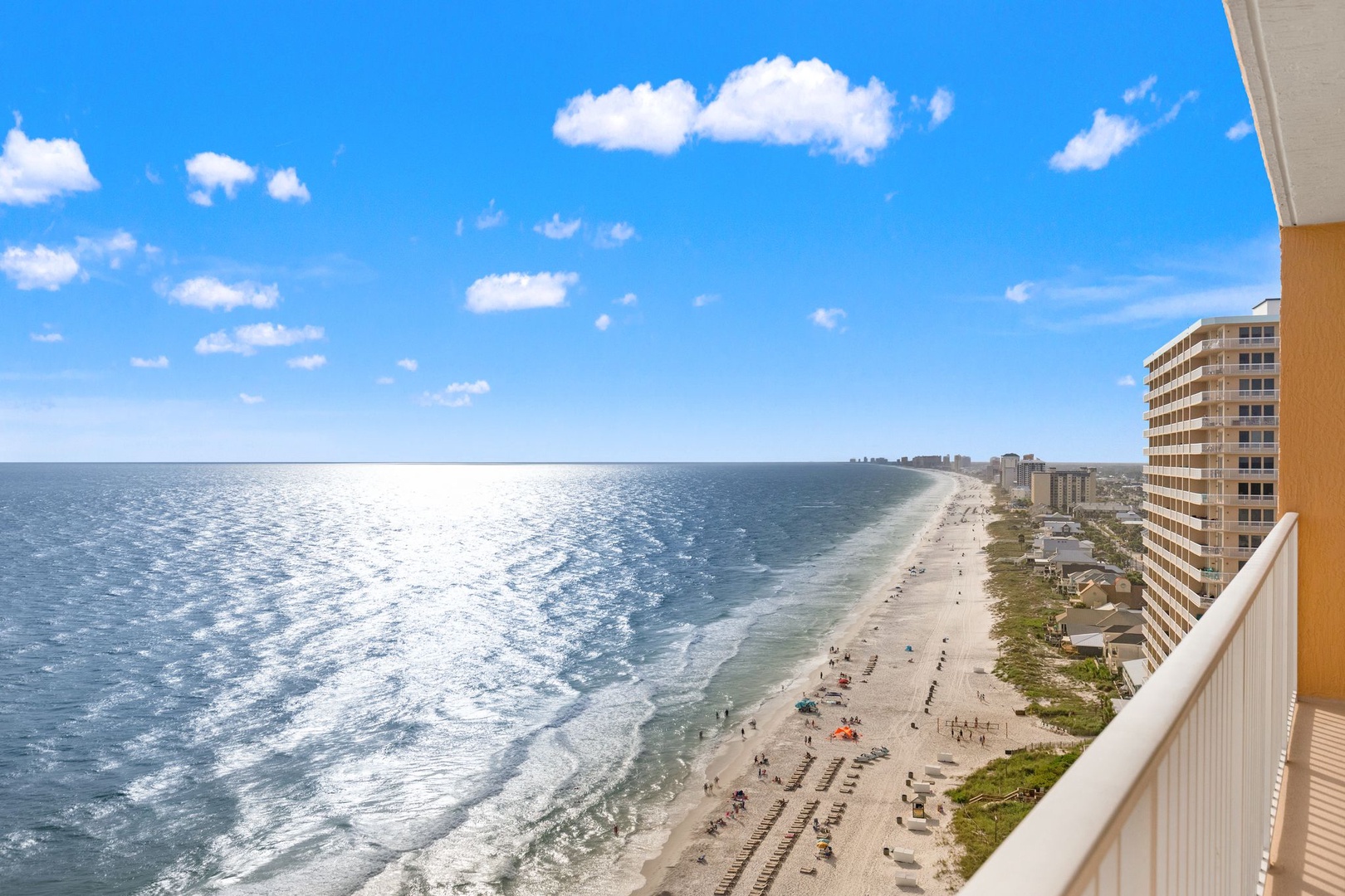 Expansive coastal views showcase a pristine sandy shoreline stretching along sparkling blue waters beneath clear skies, with neighboring beachfront properties lining the coast.