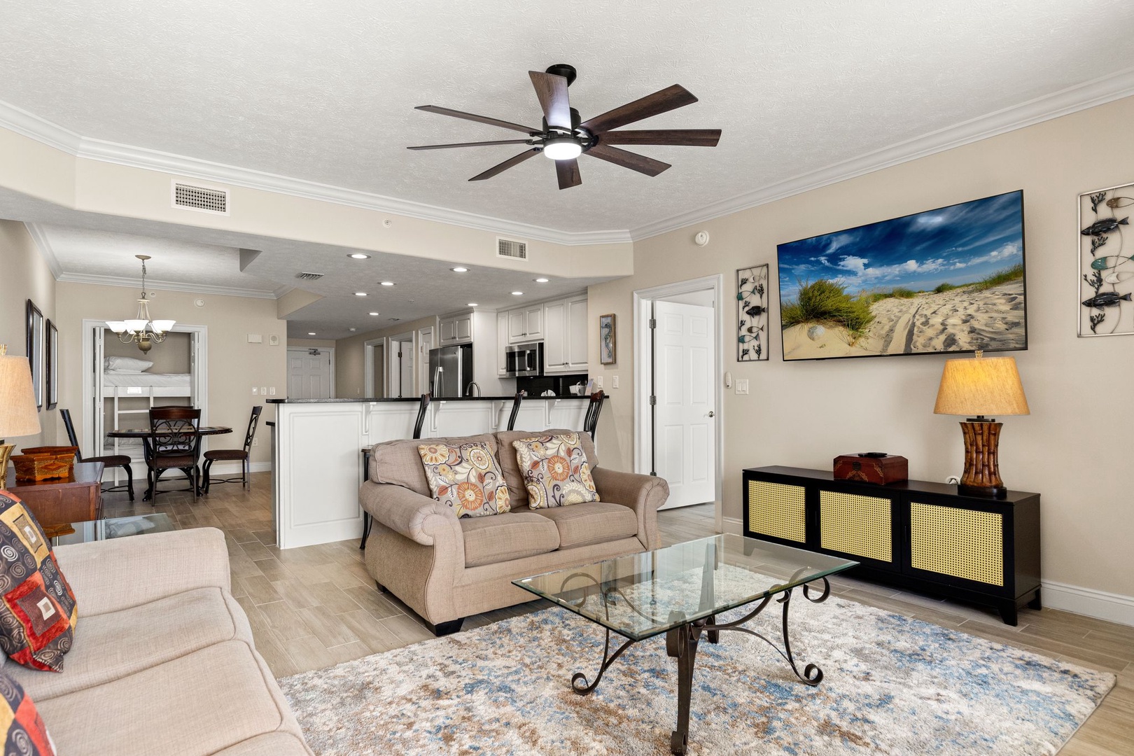 Relax in your spacious open-concept living room with comfortable seating, ceiling fan, and stunning beach artwork creating a coastal atmosphere.