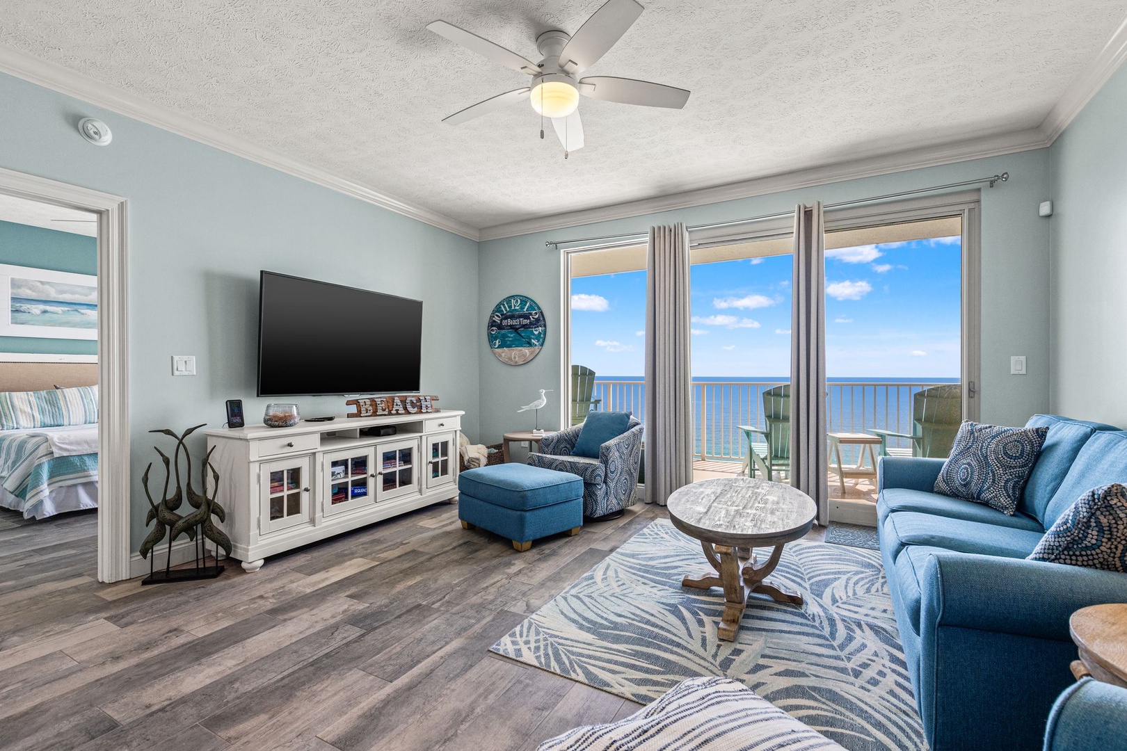 Sink into coastal comfort where ocean breezes drift through your private balcony doors. Watch waves sparkle beyond the glass as you relax on plush seating, surrounded by soothing blue tones and beach-inspired décor.